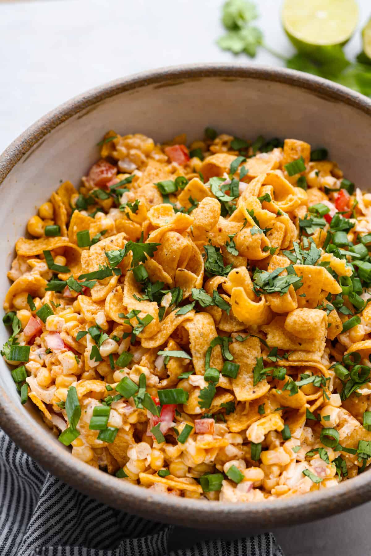 Crunchy Frito corn salad is a fun side dish bursting with Mexican-inspired flavors! Corn, cheese, peppers, and onion get tossed in a tasty dressing and mixed with Fritos corn chips. A surprising FAVORITE at any get-together! Close view of frito corn salad in a large bowl garnished with cilantro and green onions.