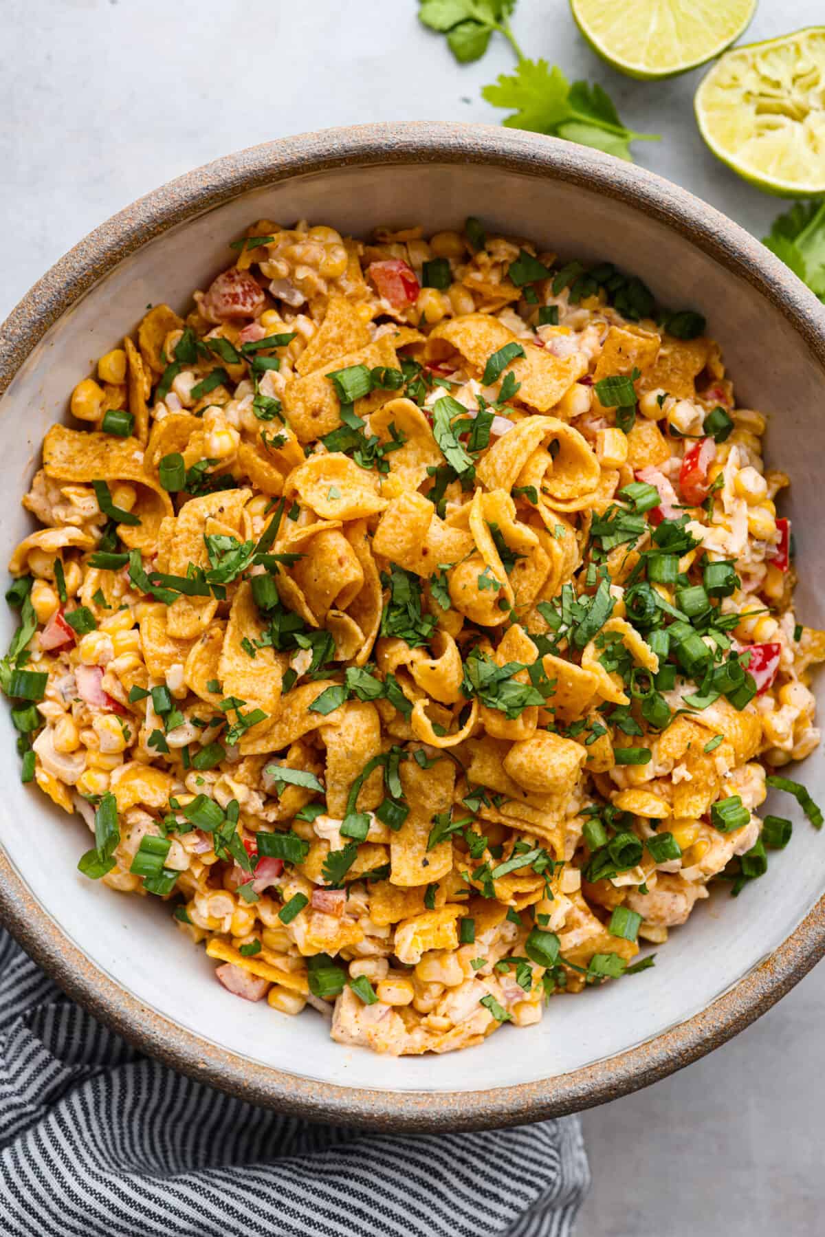 Crunchy Frito corn salad is a fun side dish bursting with Mexican-inspired flavors! Corn, cheese, peppers, and onion get tossed in a tasty dressing and mixed with Fritos corn chips. A surprising FAVORITE at any get-together! Top view of frito corn salad in a large bowl topped with corn chips, cilantro, and green onions.