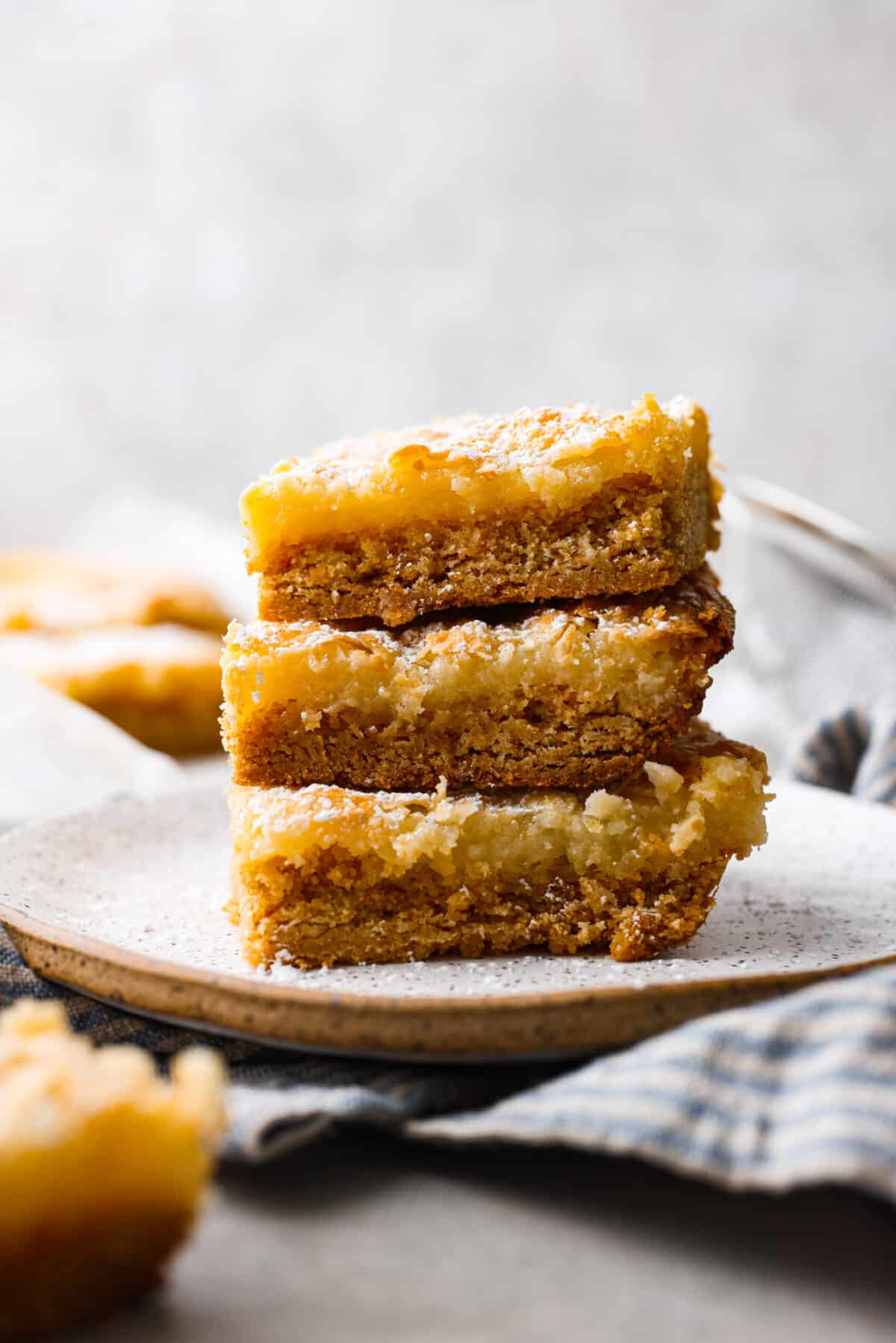 Delicious Gooey Butter Cake is an easy dessert that has a buttery cake crust and a gooey cream cheese topping. Finish with a dusting of powdered sugar for an absolutely incredible treat! Only 7 ingredients and just 15 minutes of hands-on time are required! It's perfect for any occasion and will be the star of your next gathering! 3 slices of butter cake stacked on top of each other.