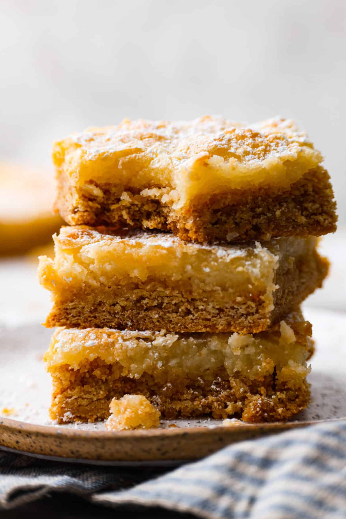 Delicious Gooey Butter Cake is an easy dessert that has a buttery cake crust and a gooey cream cheese topping. Finish with a dusting of powdered sugar for an absolutely incredible treat! Only 7 ingredients and just 15 minutes of hands-on time are required! It's perfect for any occasion and will be the star of your next gathering! Closeup of a stack of butter cake slices.