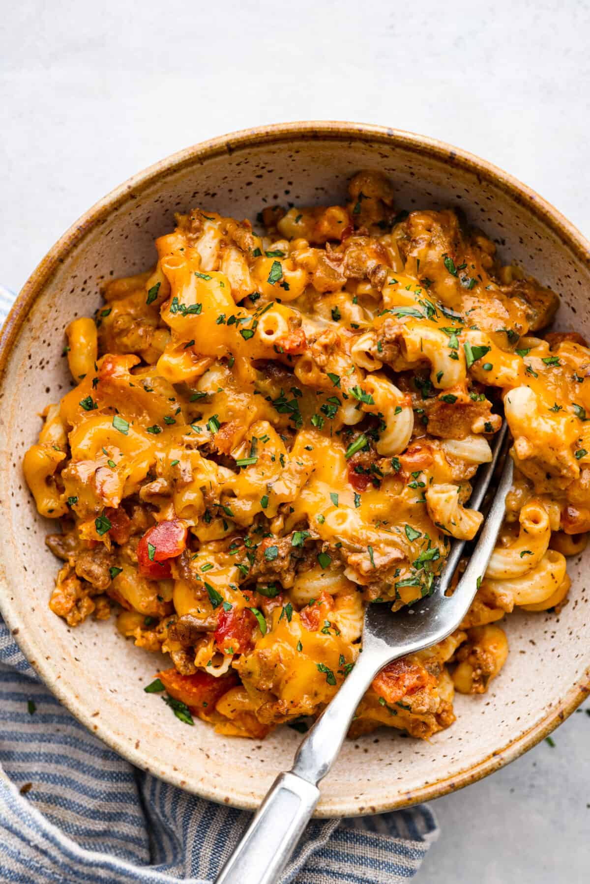 Cheeseburger Casserole has all of those delicious cheeseburger flavors in one easy-to-make dish! Loaded with ground beef, veggies, dill relish, pasta and plenty of cheese, all baked together for a comforting family-friendly dinner. Cheeseburger casserole served in a stoneware dish.
