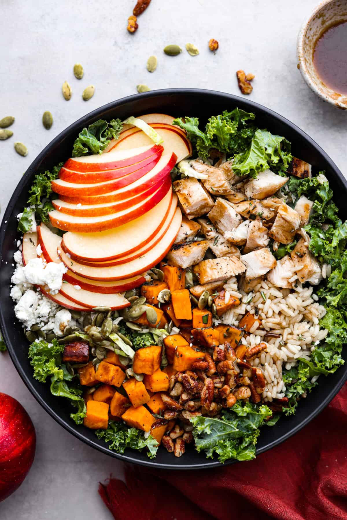 This gorgeous Harvest Bowl has all the most delicious flavors of fall packed in one easy salad. It’s filled with creamy sweet potatoes, kale, Brussels sprouts, wild rice, grilled chicken, sweet apple, cheese, crunchy candied pecans, and pepitas with the best balsamic vinaigrette dressing. You'll be craving it all season long! Top-down view of a salad made with kale, apples, chicken, wild rice, sweet potatoes, pecans, and goat cheese.