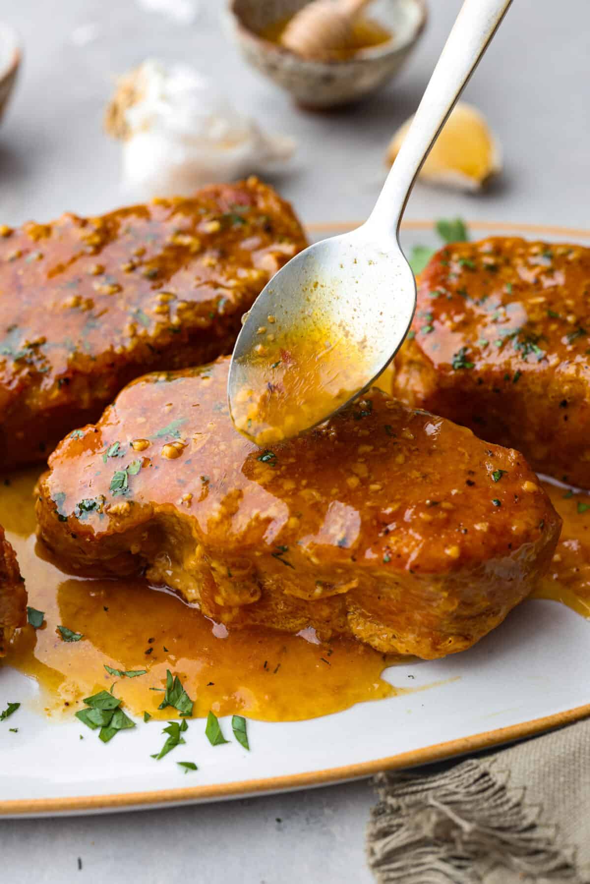 These slow cooker honey garlic pork chops are incredibly tender, they practically melt in your mouth! Cooked in a sweet and savory sauce, you won't be able to stop after one bite. Spooning honey garlic sauce over a pork chop.