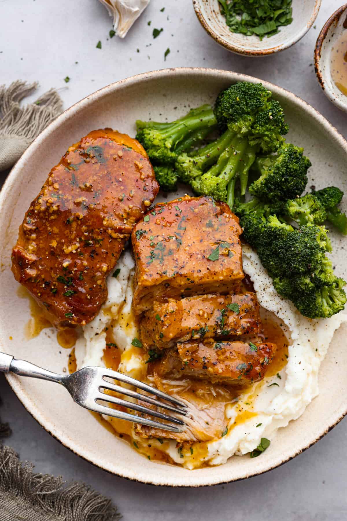 These slow cooker honey garlic pork chops are incredibly tender, they practically melt in your mouth! Cooked in a sweet and savory sauce, you won't be able to stop after one bite. A sliced pork chop served with broccoli and mashed potatoes.