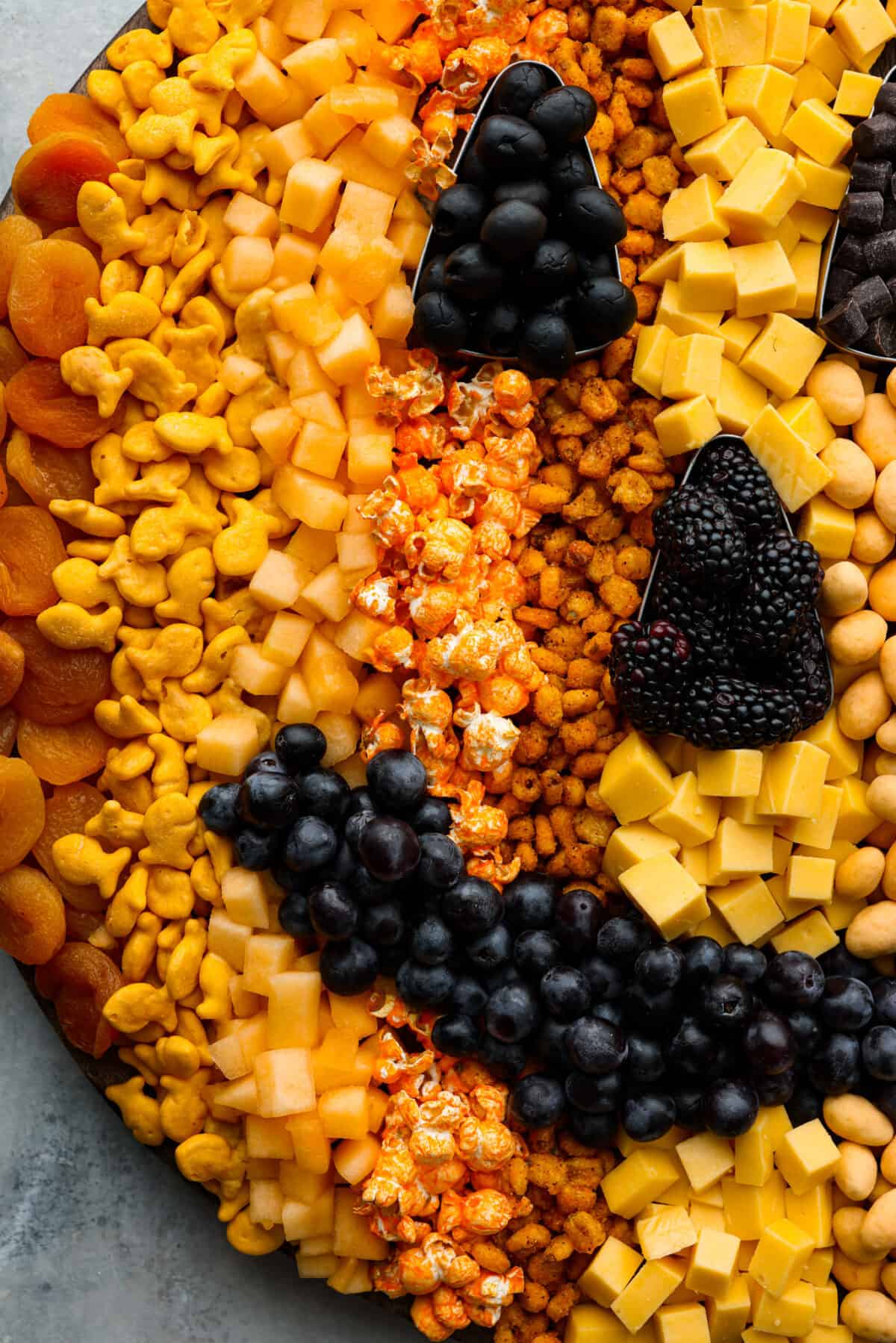 Halloween is the BEST time to get creative and have fun with your food! Gather all things orange and bring this pumpkin charcuterie board to your next fall get-together. Fill your board to look like a Jack-o-lantern; it will be the talk of the party! Close view of fruit, crackers, and popcorn on the pumpkin charcuterie board.