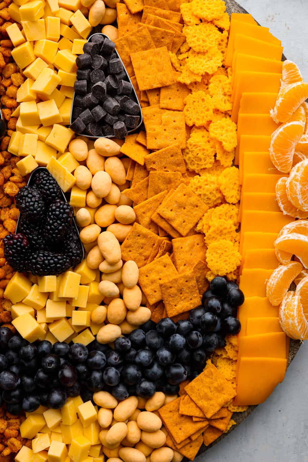 Halloween is the BEST time to get creative and have fun with your food! Gather all things orange and bring this pumpkin charcuterie board to your next fall get-together. Fill your board to look like a Jack-o-lantern; it will be the talk of the party! Close view of crackers, cheese, fruit, and candy on the pumpkin charcuterie board.