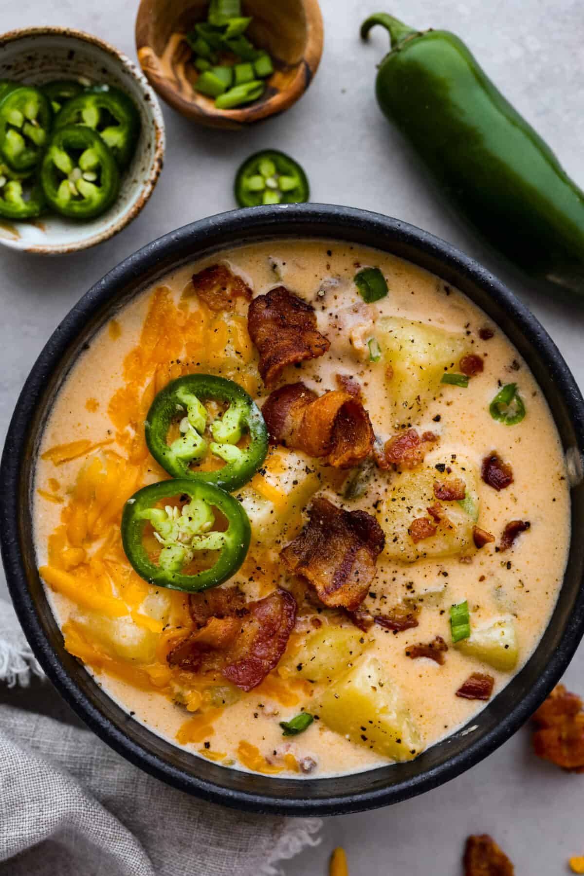 A classic appetizer made into a hearty soup! Creamy, cheesy, and packed with potatoes, jalapenos, and bacon, this jalapeno popper soup is the perfect comfort food for lower temperatures. Soup served in a black bowl, surrounded by jalapeños.
