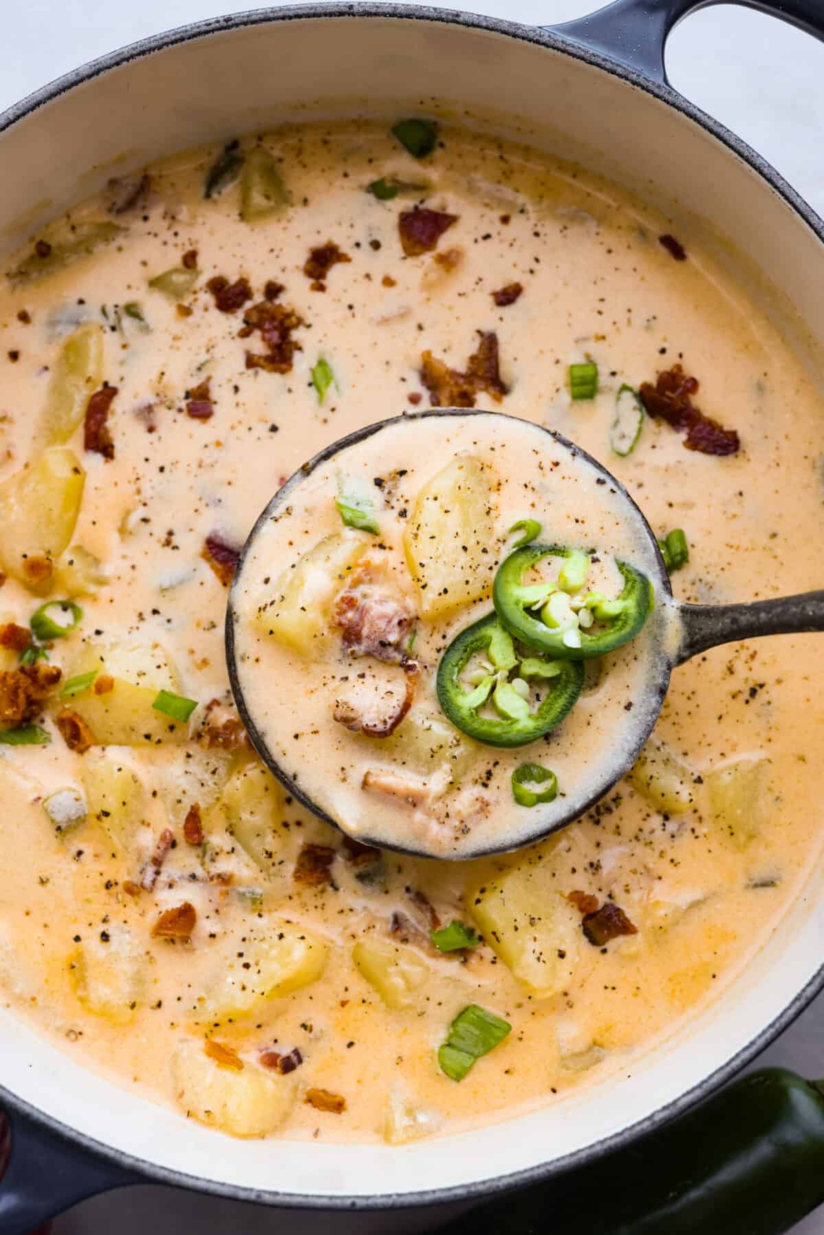 A classic appetizer made into a hearty soup! Creamy, cheesy, and packed with potatoes, jalapenos, and bacon, this jalapeno popper soup is the perfect comfort food for lower temperatures. Scooping the soup out of a large blue and white pot using a ladle.
