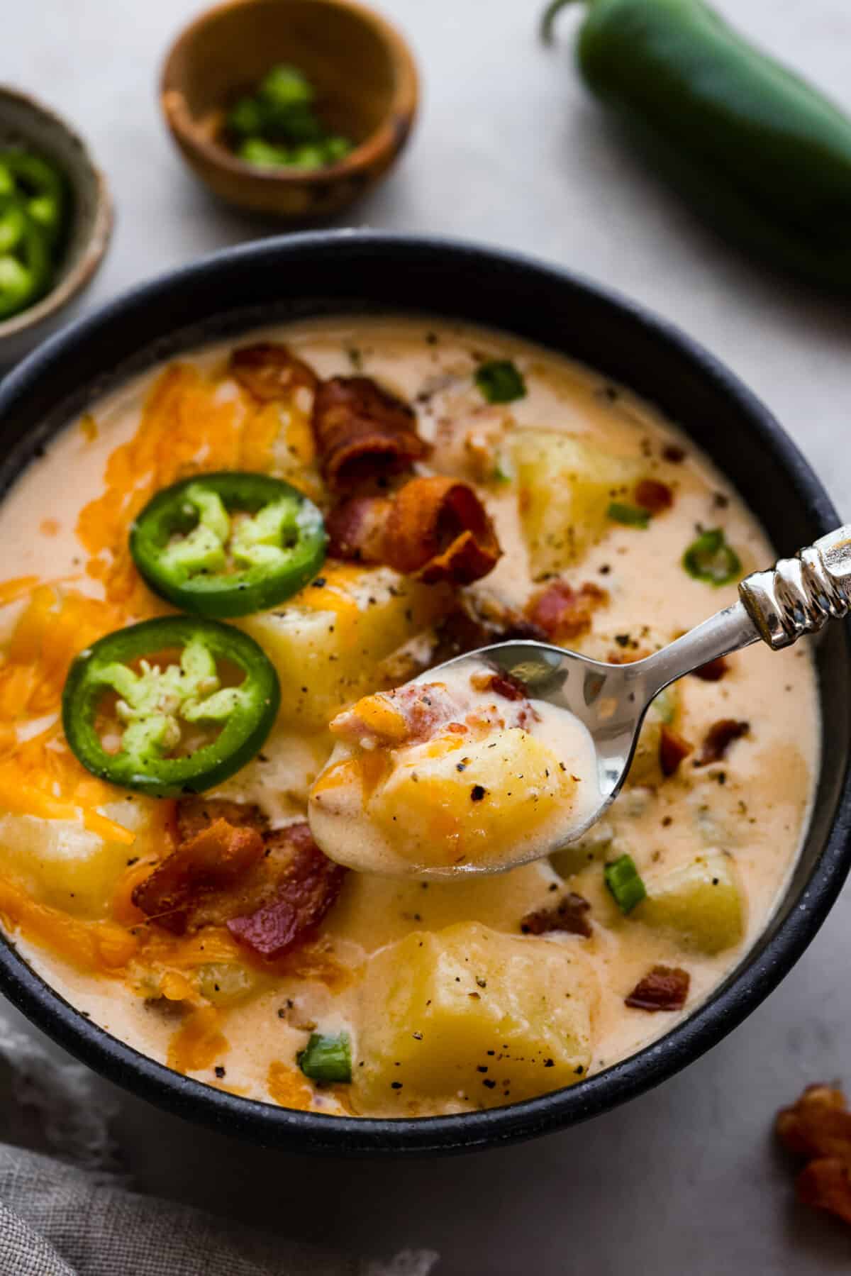 A classic appetizer made into a hearty soup! Creamy, cheesy, and packed with potatoes, jalapenos, and bacon, this jalapeno popper soup is the perfect comfort food for lower temperatures. Closeup of a serving of jalapeno popper soup in a black bowl.