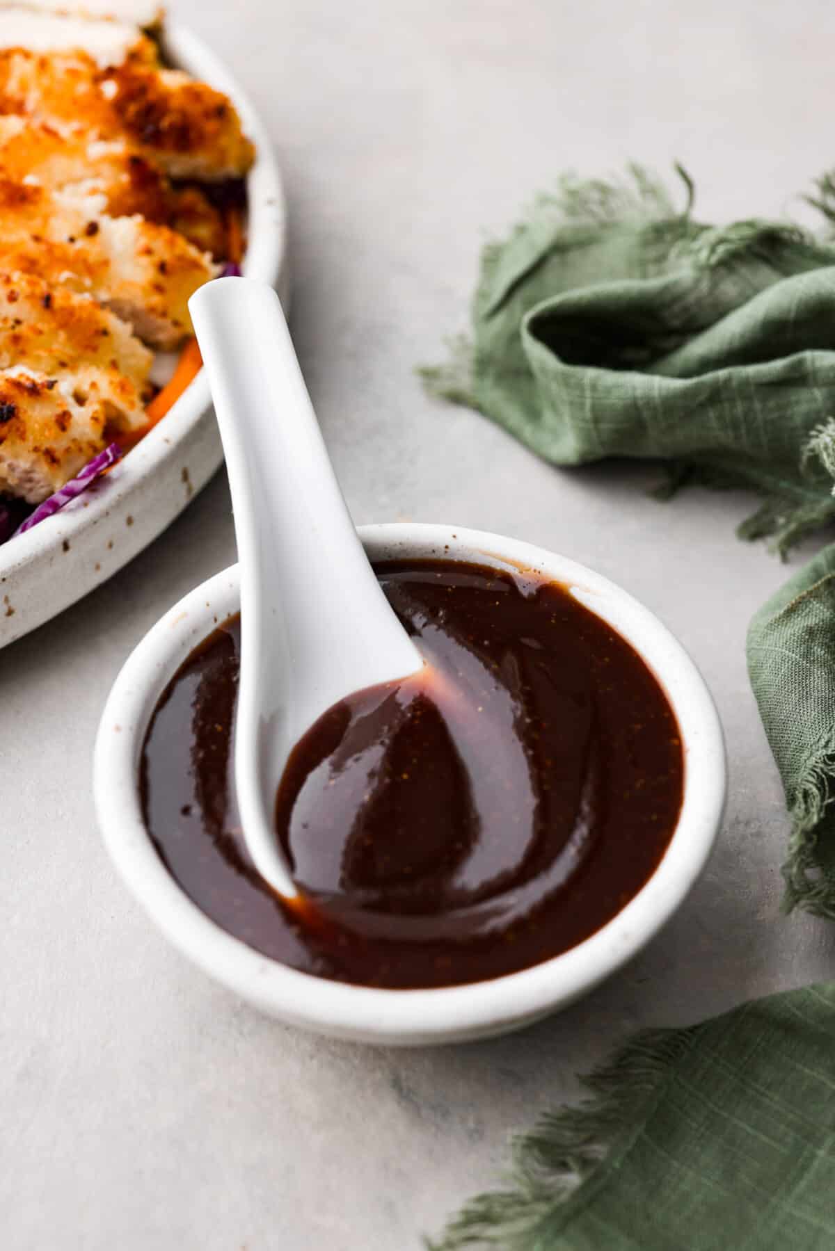 Katsu sauce is a thick and glossy ketchup-based sauce that's perfect for dipping fried foods in! A staple in Japanese and Hawaiian cuisine, you're going to love having this on hand in your kitchen. A large white spoon inside a small bowl of katsu sauce.