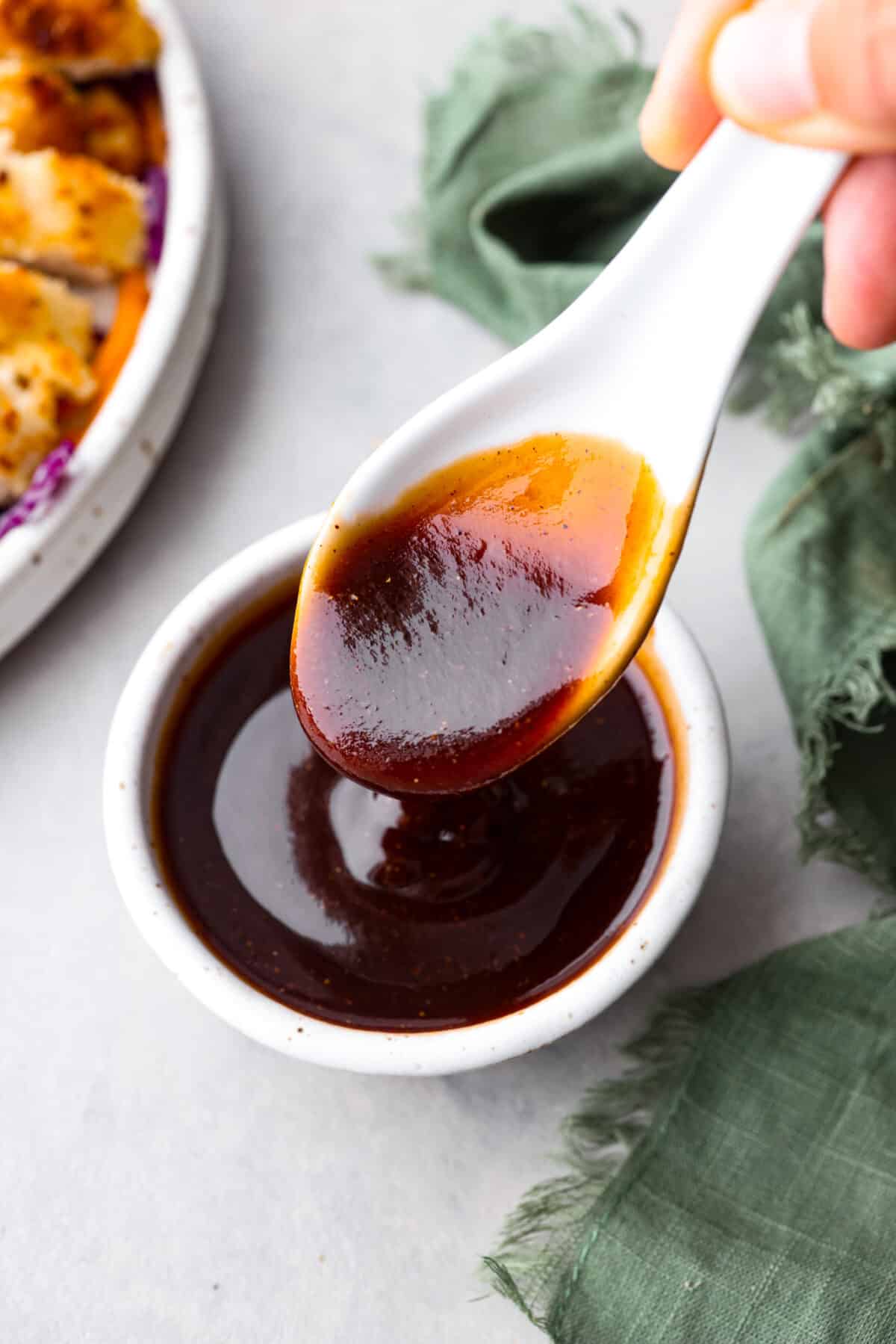 Katsu sauce is a thick and glossy ketchup-based sauce that's perfect for dipping fried foods in! A staple in Japanese and Hawaiian cuisine, you're going to love having this on hand in your kitchen. A small white bowl filled with homemade katsu sauce, being served with a large soup spoon.