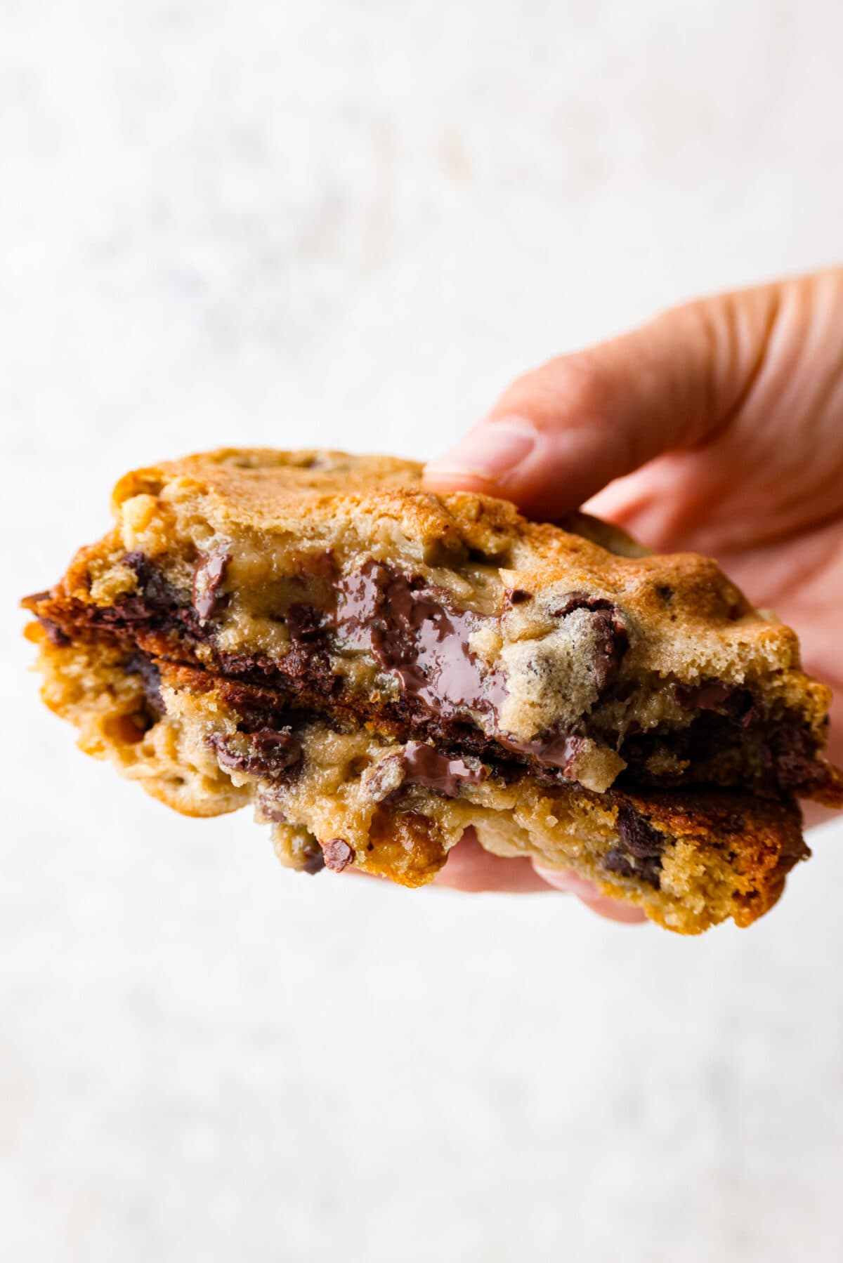 New York City's most beloved cookie, the Levain Cookie is perfectly crisp around the edges with an irresistible thick and gooey center. Picking up a copycat levain cookie that has been broken in half.