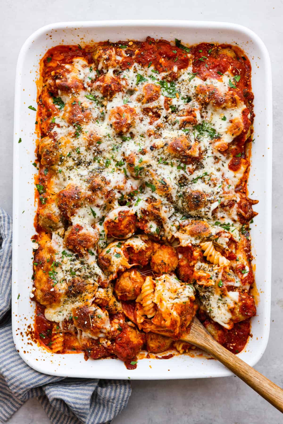 With just one dish to wash and a handful of simple ingredients, you can treat your entire family to this hearty meatball casserole. It has tender meatballs nestled in a bed of rotini pasta, smothered in marinara sauce, and topped with gooey mozzarella and parmesan cheese. Top-down view of meatball casserole in a white baking dish.