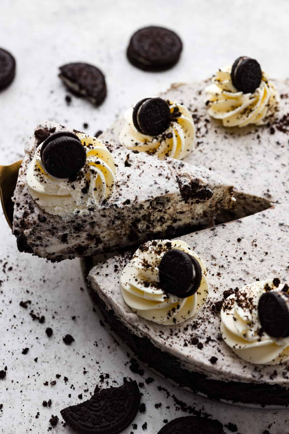 Indulge in pure dessert delight with this no-bake Oreo cheesecake! It has a creamy filling packed with crushed Oreos on a crust made of even more Oreos—talk about dreamy! And the best part? It's a breeze to whip up, no need to turn on your oven! One slice cut out of a whole no bake Oreo cheesecake.