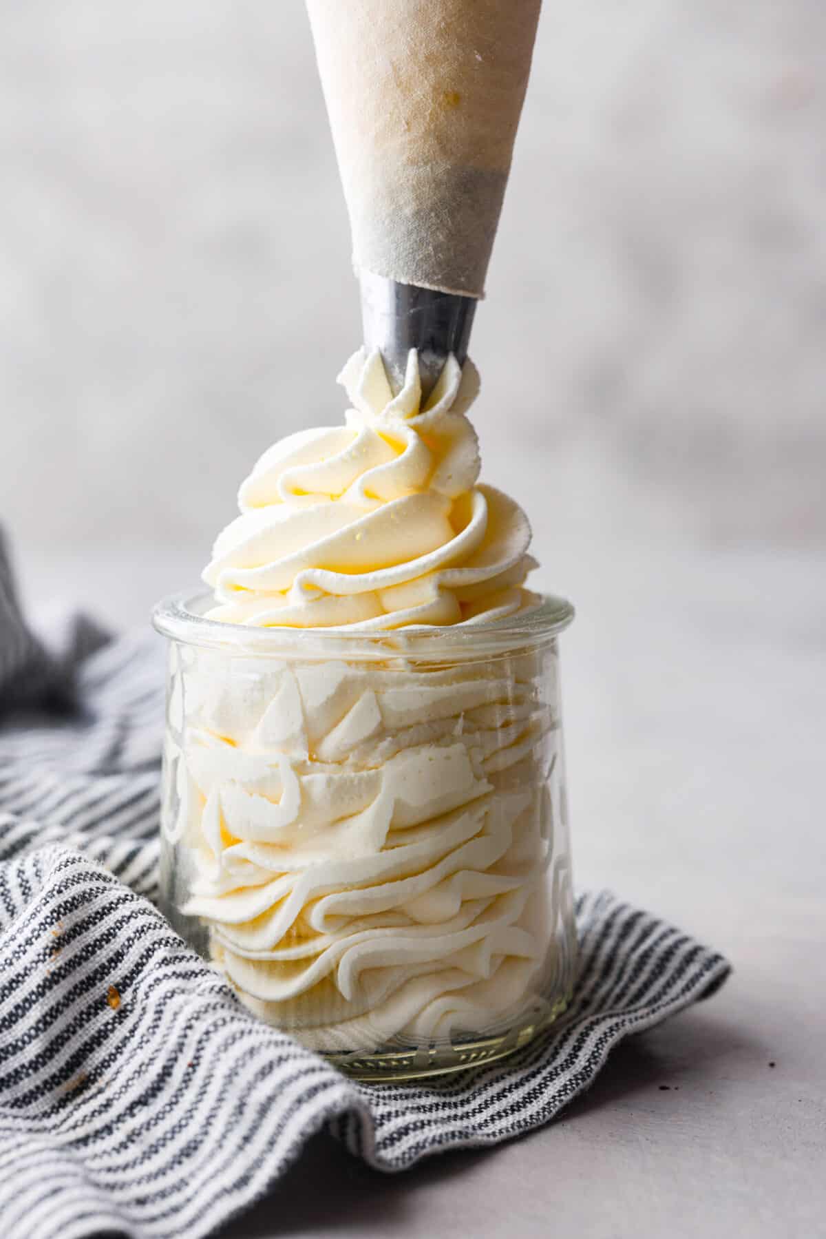 Stabilized whipped cream is fluffy and sturdy enough to keep its shape! Thicker than regular whipped cream, it's perfect for piping and frosting desserts. It's way better than Cool Whip! Side view of a piping bag piping stabilized whipped cream into a glass jar.