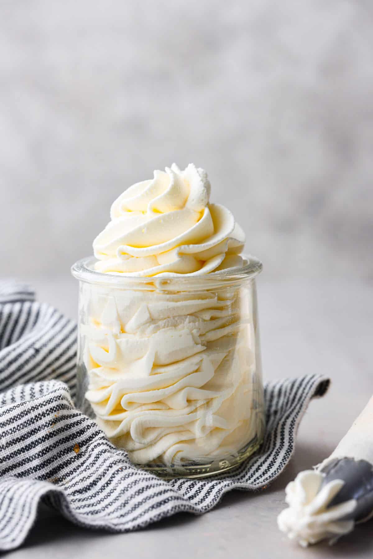 Stabilized whipped cream is fluffy and sturdy enough to keep its shape! Thicker than regular whipped cream, it's perfect for piping and frosting desserts. It's way better than Cool Whip! Close up view of stabilized whipped cream piped in a glass jar.