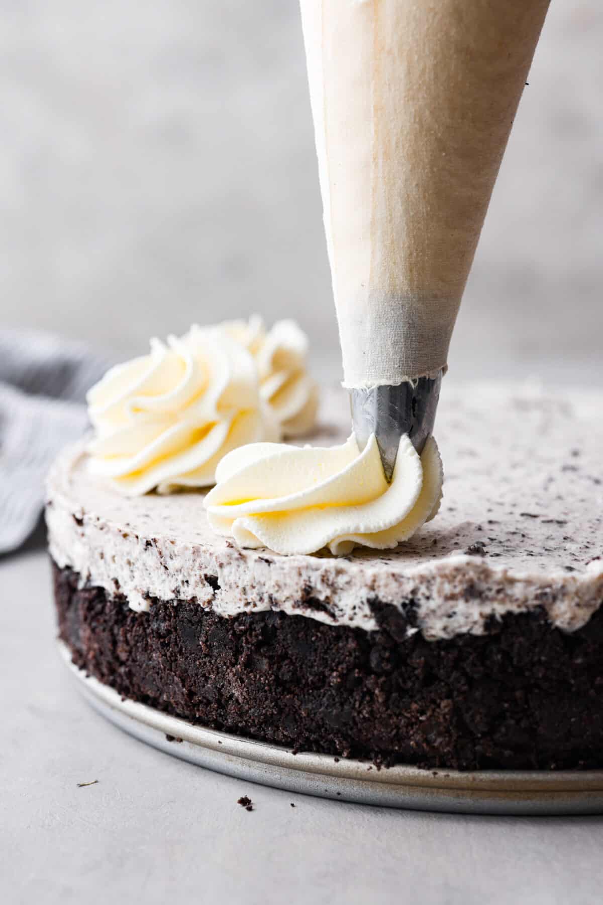 Stabilized whipped cream is fluffy and sturdy enough to keep its shape! Thicker than regular whipped cream, it's perfect for piping and frosting desserts. It's way better than Cool Whip! Close view of a piping bag piping stabilized whipped cream on an Oreo cheesecake.