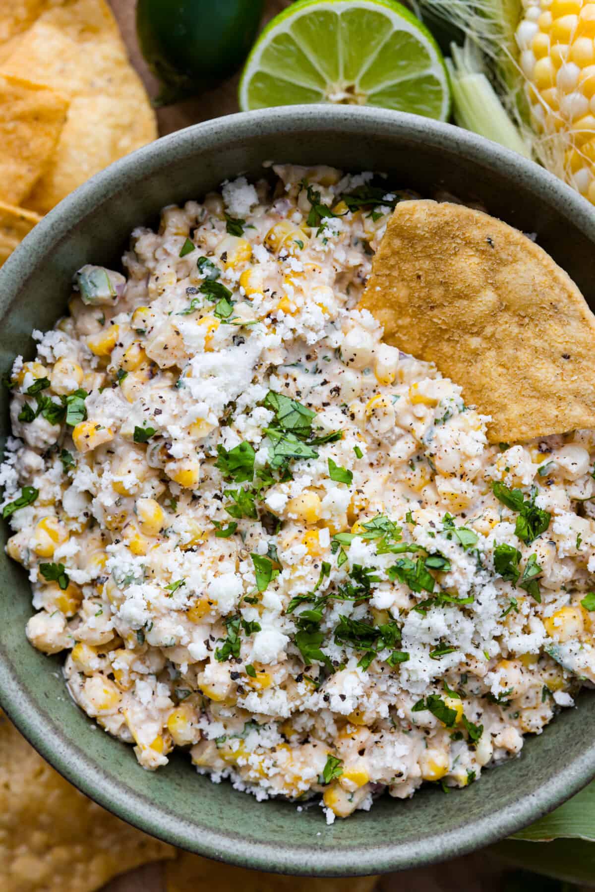 Dive into the irresistible taste of Mexican street corn with this easy-to-make dip. Charred corn, green chilies, spices, and creamy mayo blend perfectly for a delicious appetizer for any occasion! A close up of a bowl of corn dip with a tortilla chip in it.
