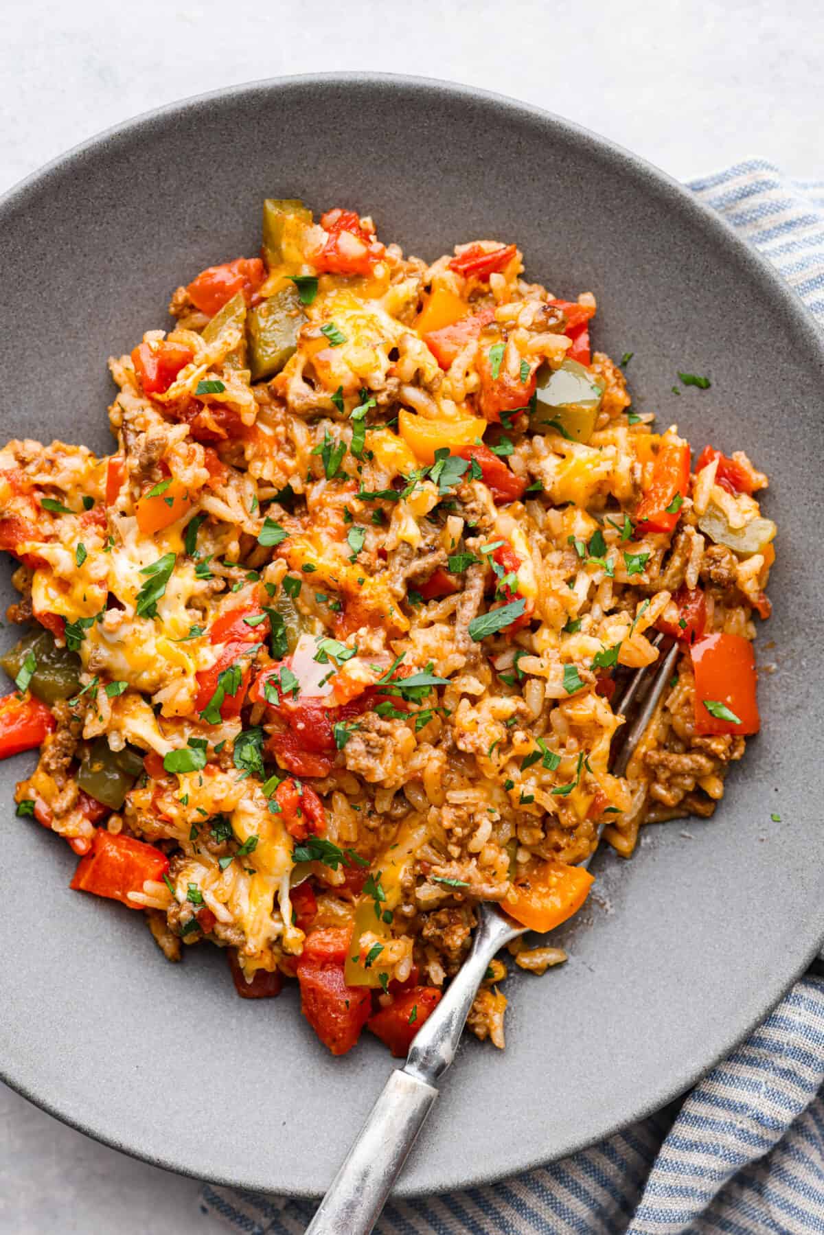 All the hearty, flavorful goodness of a stuffed pepper in one easy-to-make casserole! Stuffed pepper casserole is easy, cheesy, and packed to the brim with delicious seasoned rice and vegetables. A casserole serving in a gray dish.