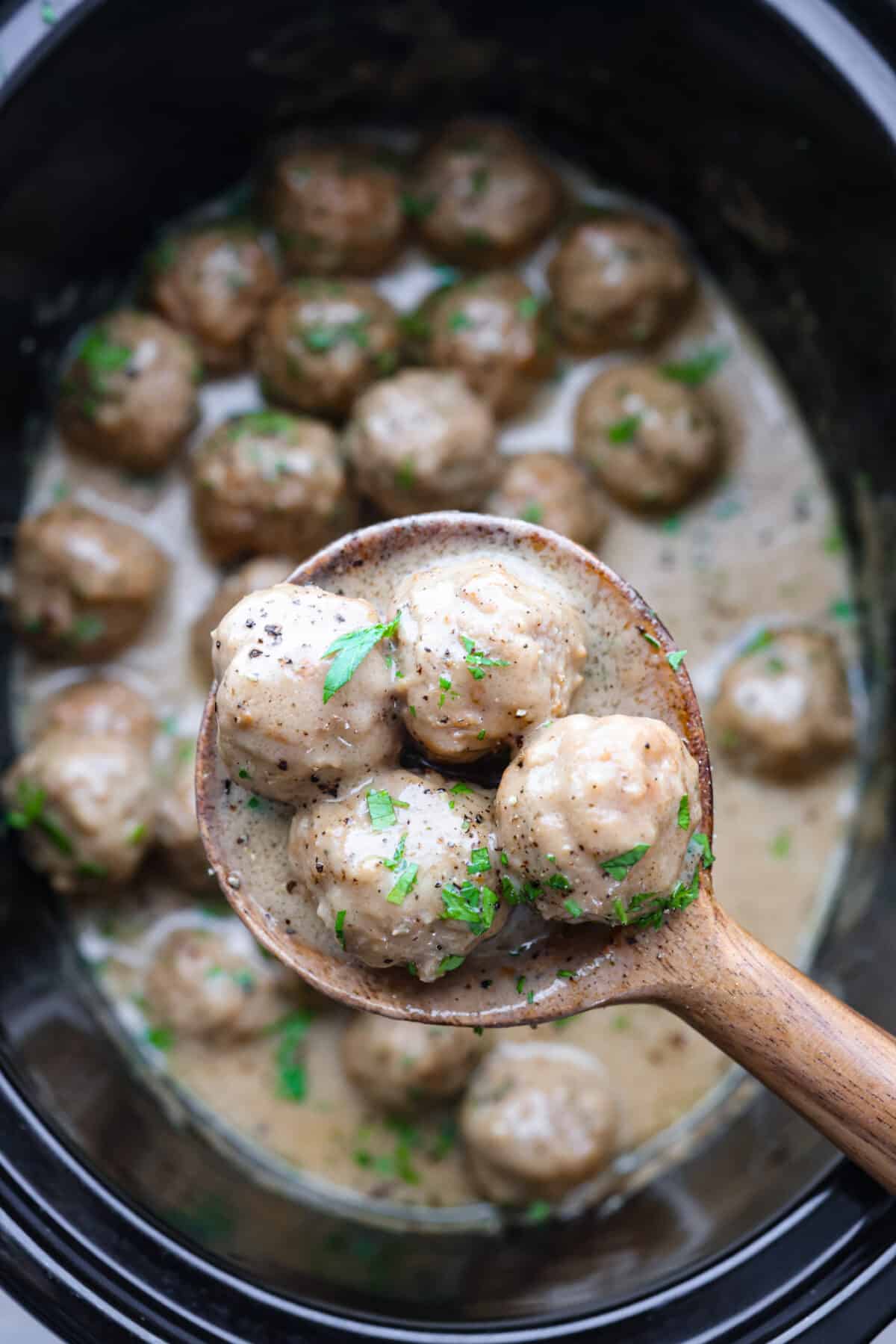 Slow cooker Swedish meatballs are braised in a rich and flavorful cream sauce. Combining ground beef, pork, and warm spices makes for the most comforting and satisfying meal. Serve as an appetizer or hearty meal. Close up shot of a scoop of slow cooker Swedish meatballs.