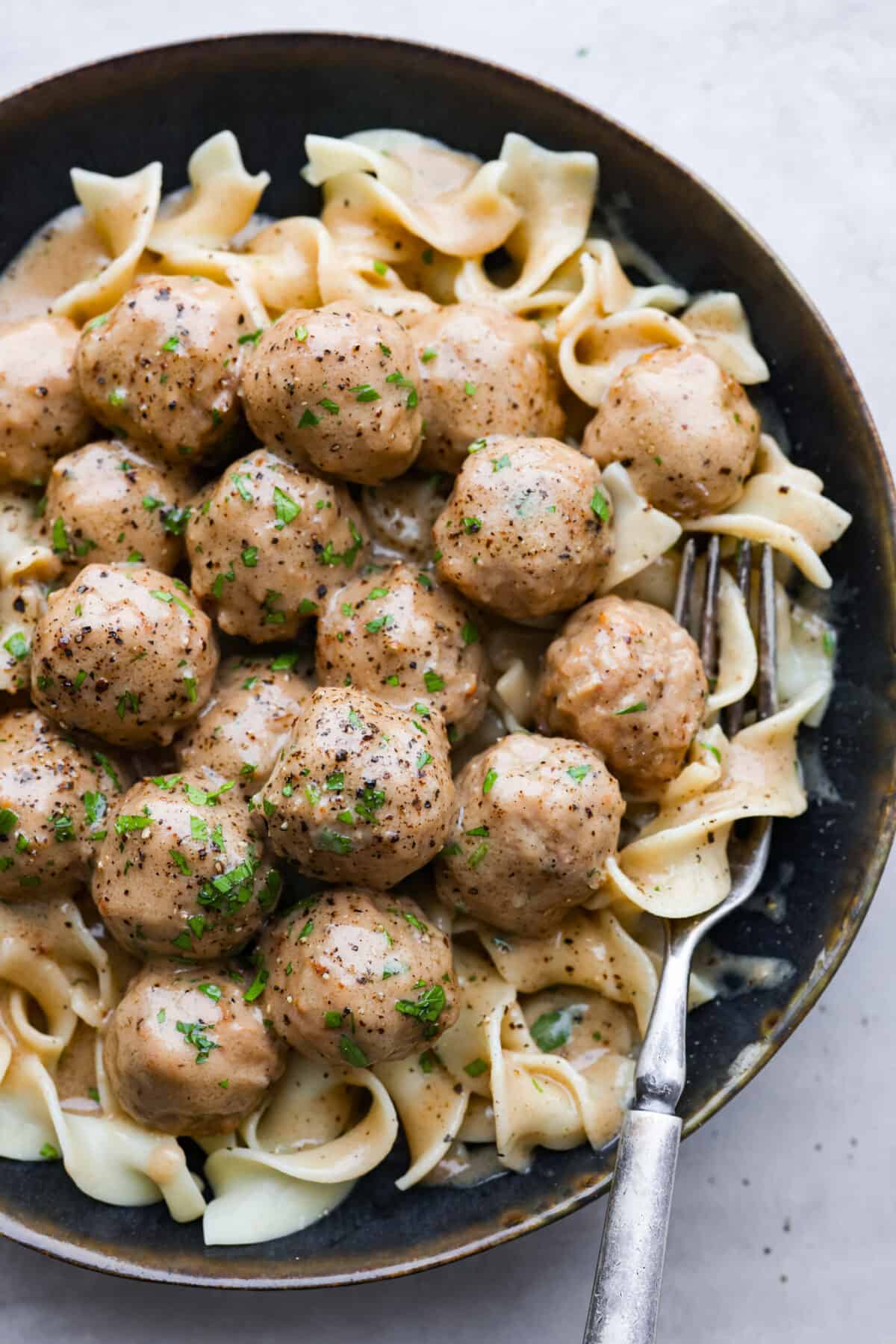 Slow cooker Swedish meatballs are braised in a rich and flavorful cream sauce. Combining ground beef, pork, and warm spices makes for the most comforting and satisfying meal. Serve as an appetizer or hearty meal. Overhead shot of plated Swedish meatballs over egg noodles.
