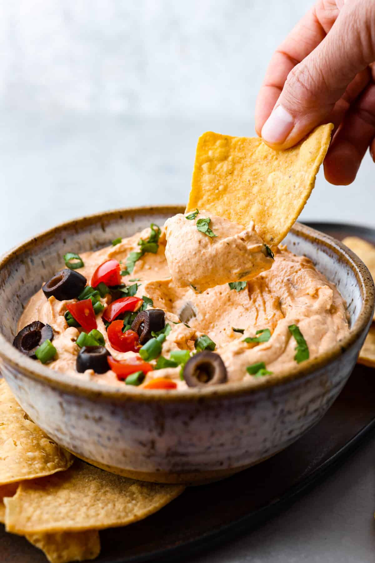 Taco dip takes all the tasty flavor of tacos and turns it into a creamy, zesty, easy-to-eat appetizer. Whip this up in 5 minutes with just 4 key ingredients. It is so deliciously addicting and will be the star of the party!ย Dipping a tortilla chip into the dip.