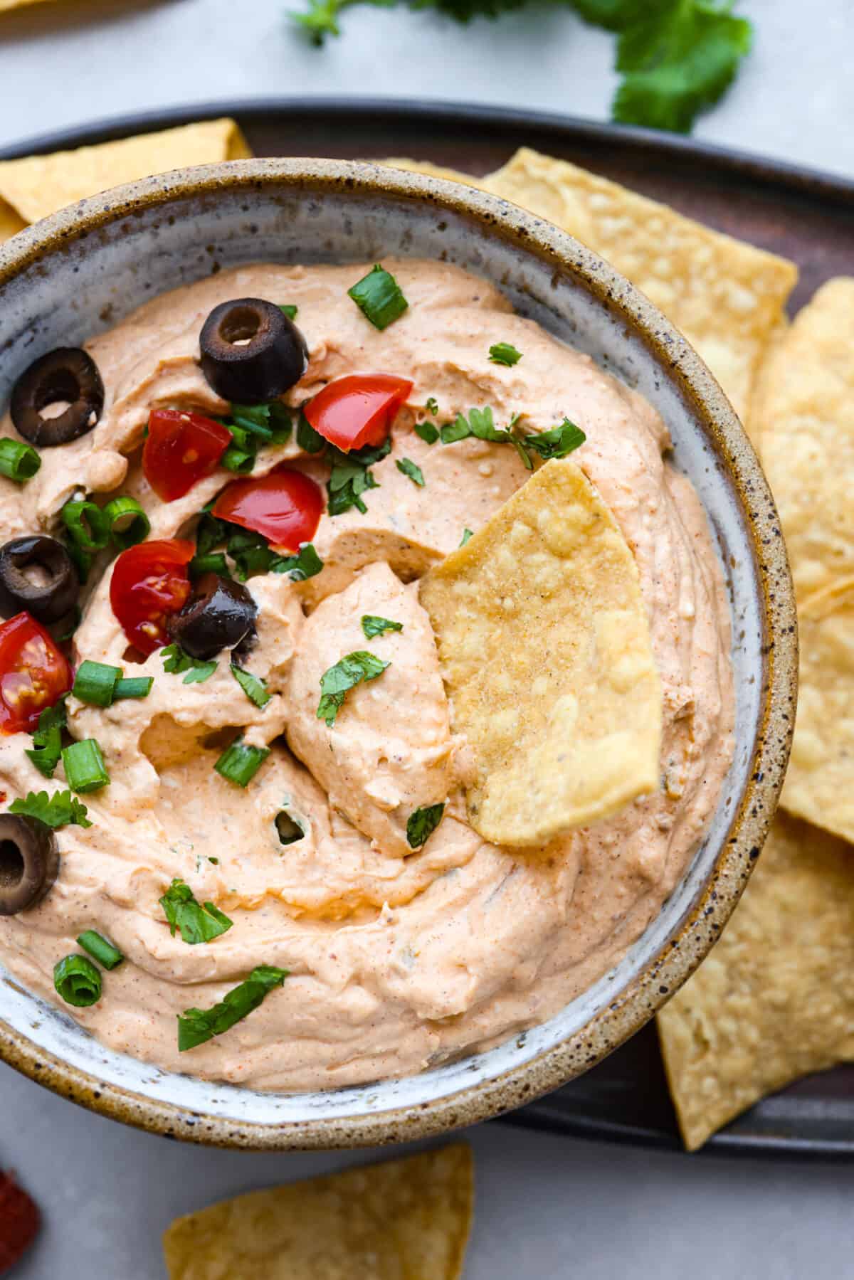 Taco dip takes all the tasty flavor of tacos and turns it into a creamy, zesty, easy-to-eat appetizer. Whip this up in 5 minutes with just 4 key ingredients. It is so deliciously addicting and will be the star of the party!ย Closeup of taco dip with a tortilla chip in it.