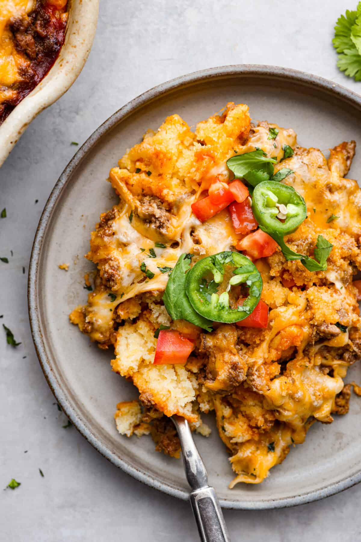 Tamale Pie is seasoned ground beef on top of a cornbread crust, drenched in a bold enchilada sauce, and topped with cheese and tomatoes. This casserole recipe is an easy spin on tamales, making it perfect for a weeknight dinner. A slice of tamale pie on a plate with a silver fork.