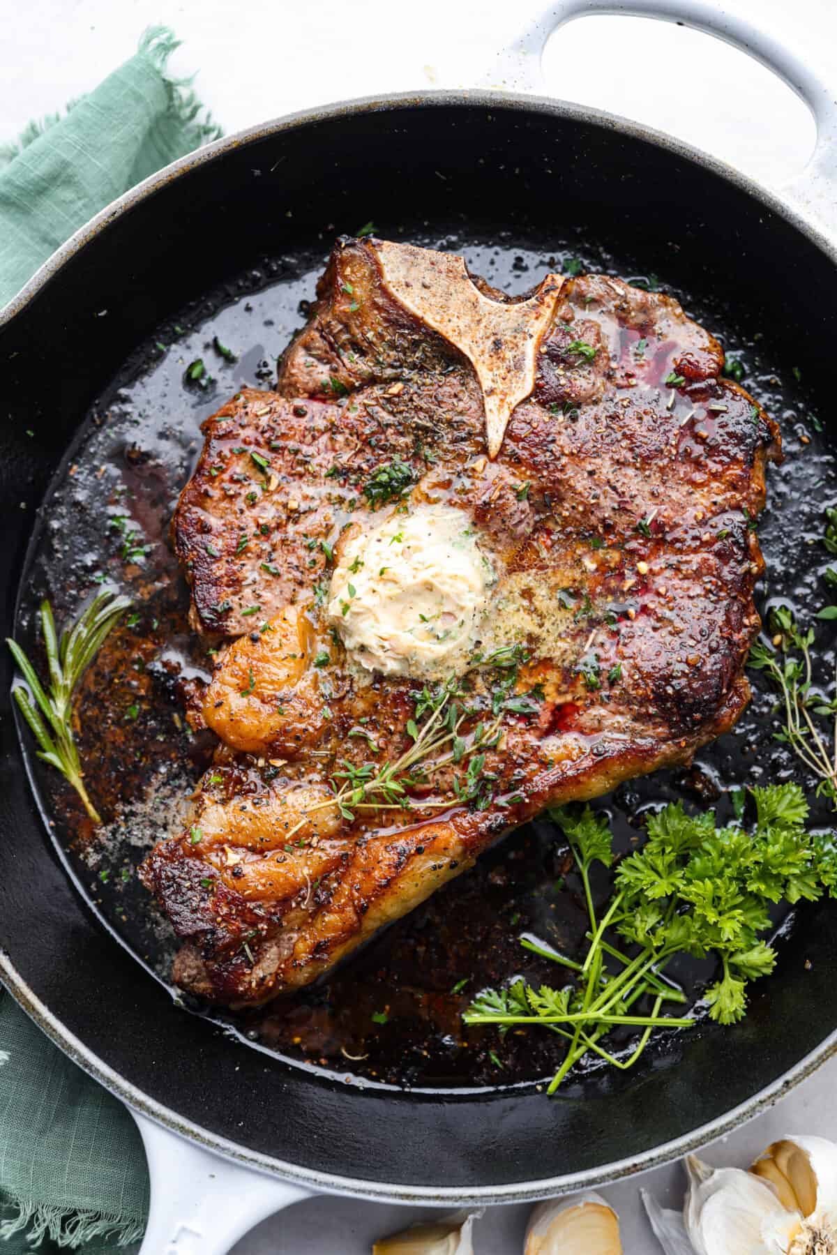 Indulge in the ultimate T-bone steak experience with this recipe! It takes an already awesome cut of meat and cooks it to perfection. The mix of olive oil, spices, and a hot skillet gives you a beautifully seared crust. Top it off with some garlic butter and fresh herbs, then you have the perfect meal ready for any occasion! A cooked t-bone steak, topped with herbs and butter in a skillet.