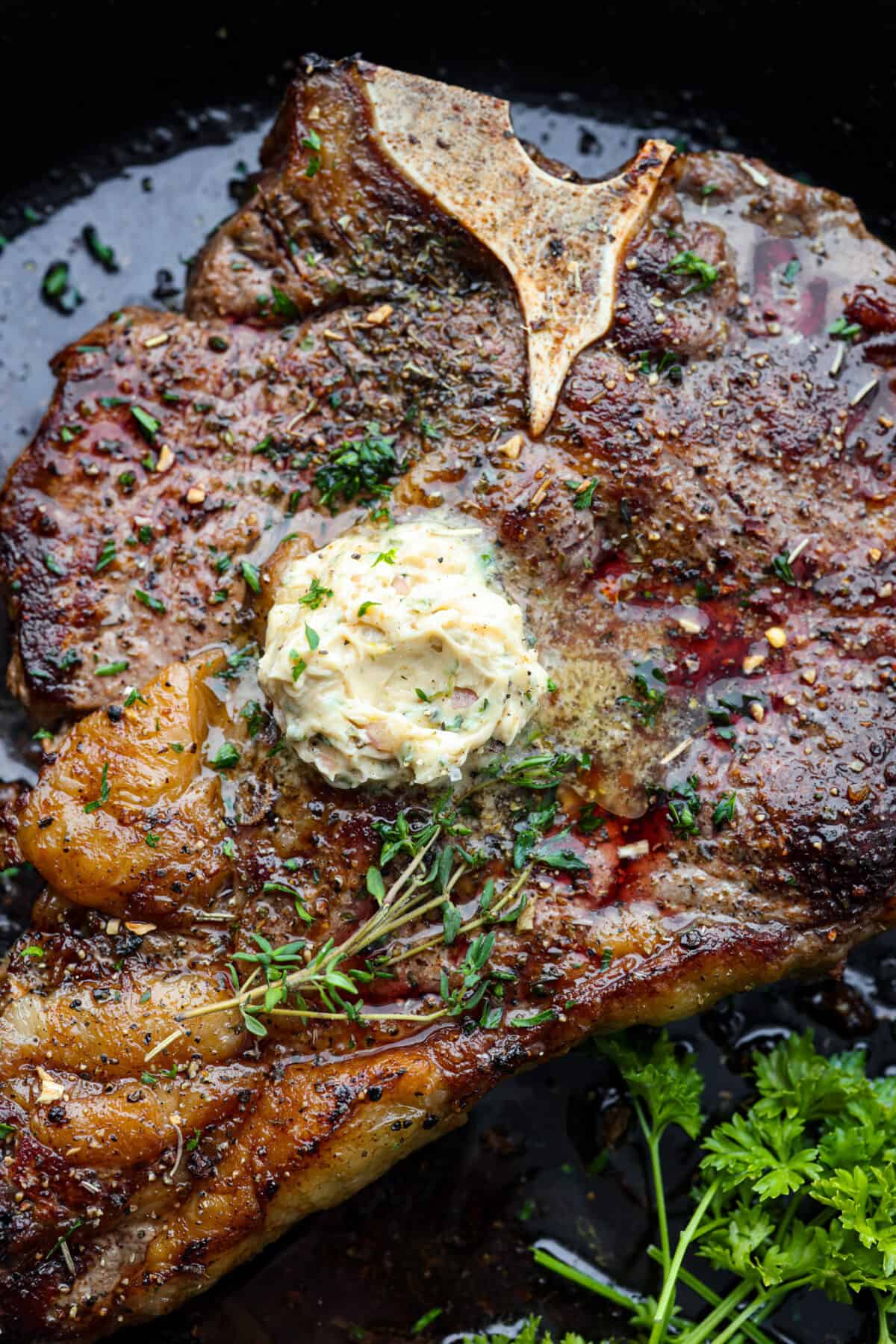 Indulge in the ultimate T-bone steak experience with this recipe! It takes an already awesome cut of meat and cooks it to perfection. The mix of olive oil, spices, and a hot skillet gives you a beautifully seared crust. Top it off with some garlic butter and fresh herbs, then you have the perfect meal ready for any occasion! Top-down view of steak topped with butter and herbs.
