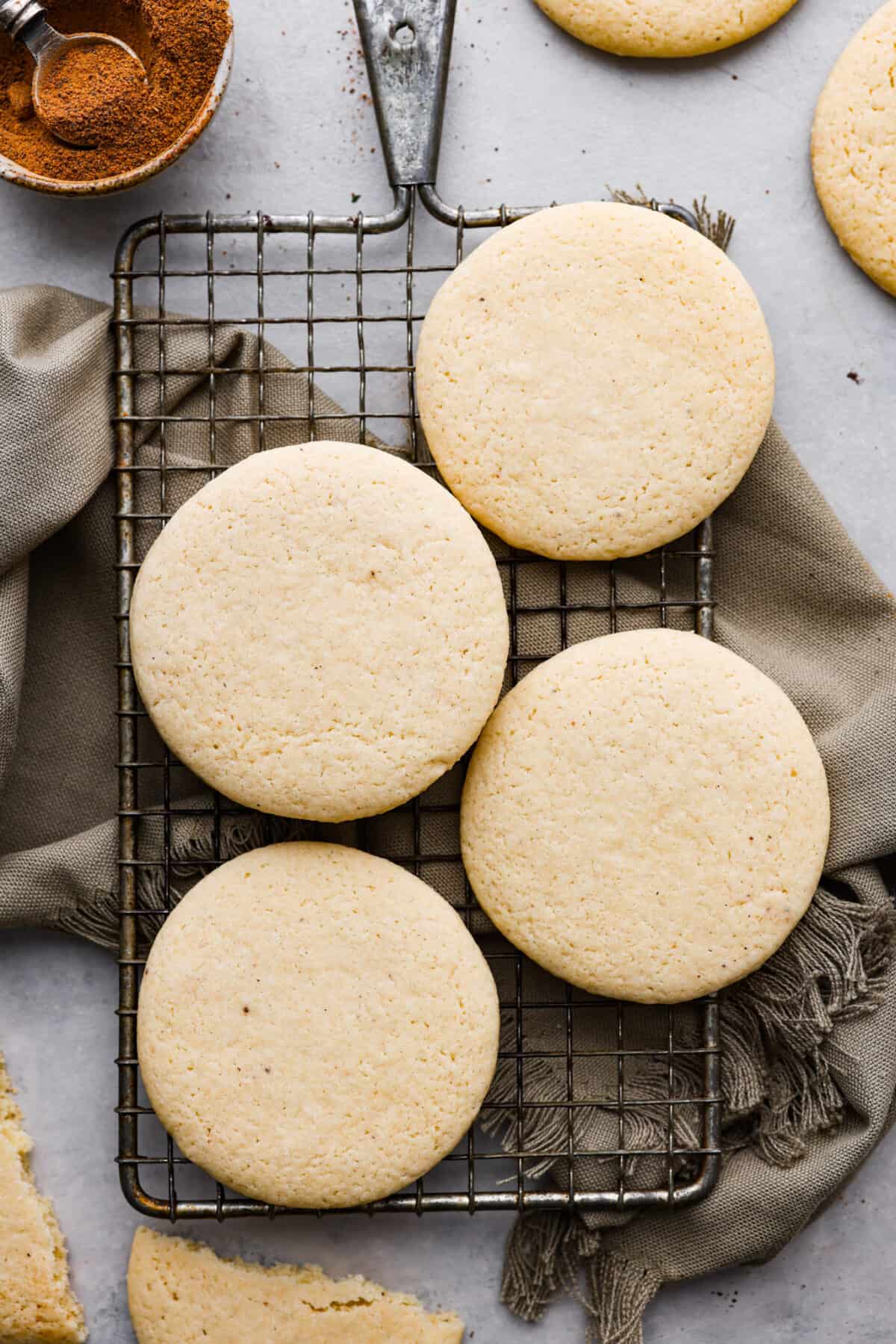 Delicately crumbly and a little bit sweet, these tea cakes are the perfect afternoon snack! They're super simple, but so irresistible. Make a cup of your favorite tea to serve with them and enjoy! Overhead shot of tea cakes on a cooling rack over a tea towel.