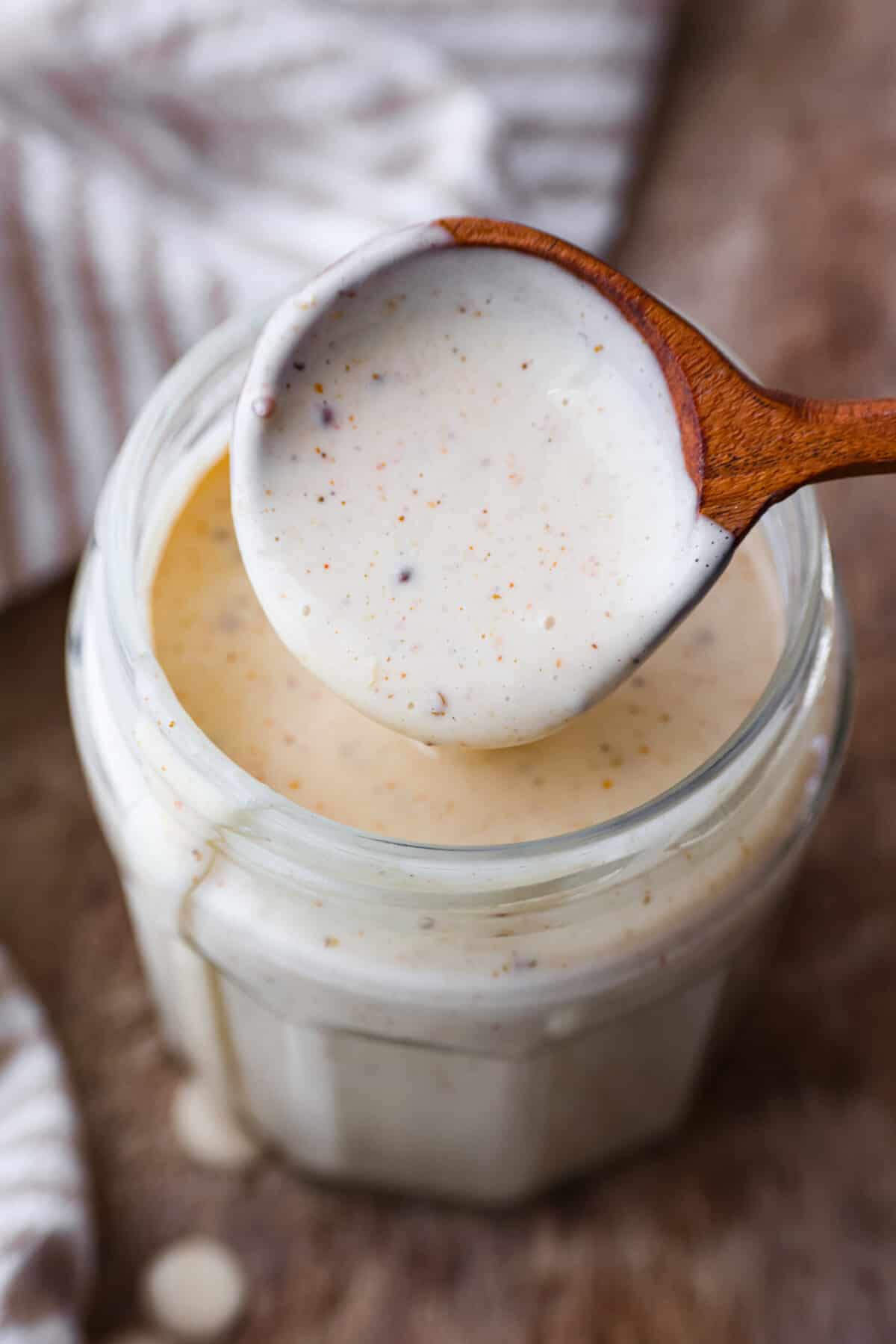 Explore the taste of the South with this easy White BBQ Sauce recipe. With just a handful of ingredients, including mayonnaise, vinegar, and spices, this creamy and tangy sauce adds a flavorful twist to your favorite veggies, fries, or chicken! A close up of Alabama White BBQ Sauce on a wooden spoon.
