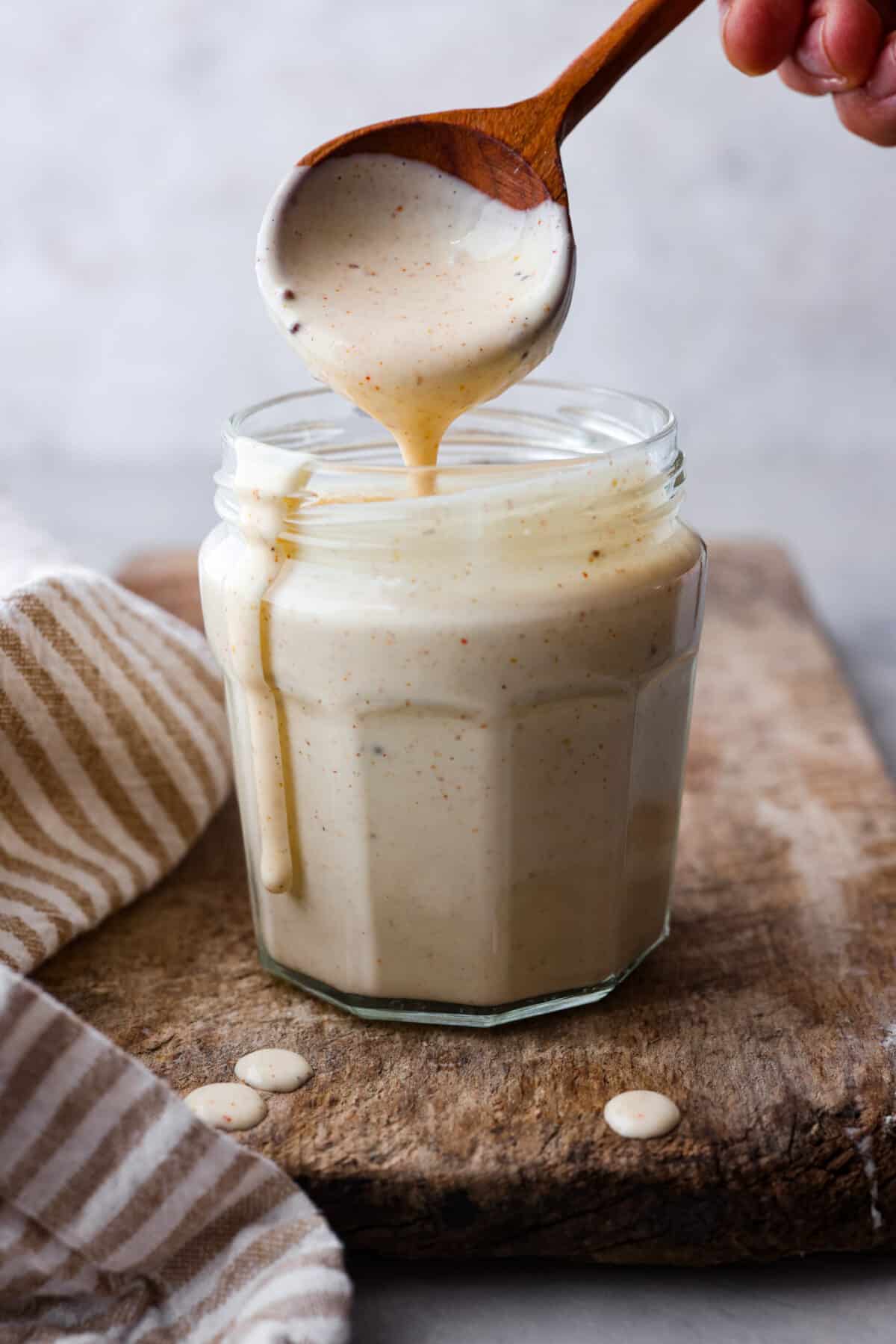 Explore the taste of the South with this easy White BBQ Sauce recipe. With just a handful of ingredients, including mayonnaise, vinegar, and spices, this creamy and tangy sauce adds a flavorful twist to your favorite veggies, fries, or chicken! A jar of Alabama White BBQ Sauce with a wooden spoon scooping some out.