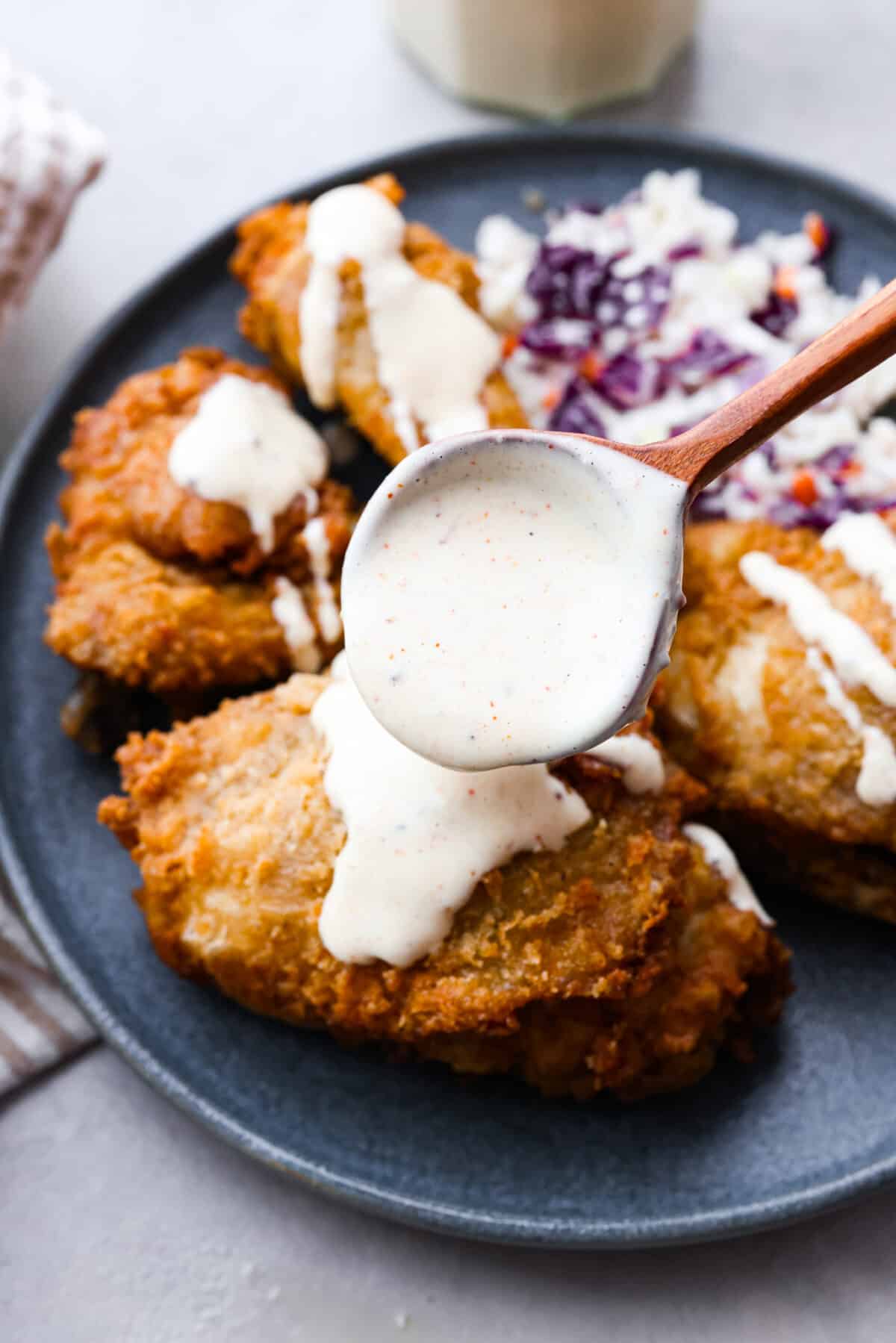 Explore the taste of the South with this easy White BBQ Sauce recipe. With just a handful of ingredients, including mayonnaise, vinegar, and spices, this creamy and tangy sauce adds a flavorful twist to your favorite veggies, fries, or chicken! The sauce being drizzled on fried chicken.