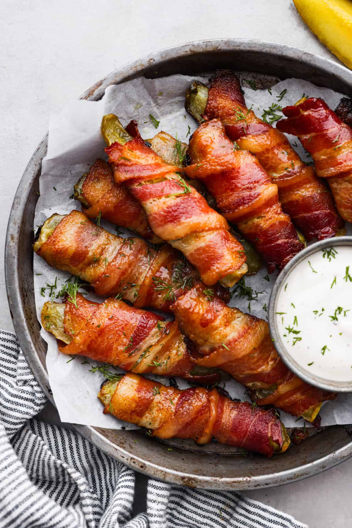 Calling all pickle lovers! Meet your new favorite appetizer. These bacon wrapped pickles are the perfect combination of tangy, crunchy, and meaty, and so easy to devour! Bacon wrapped pickles in a gray serving bowl, served with a side of ranch dressing.