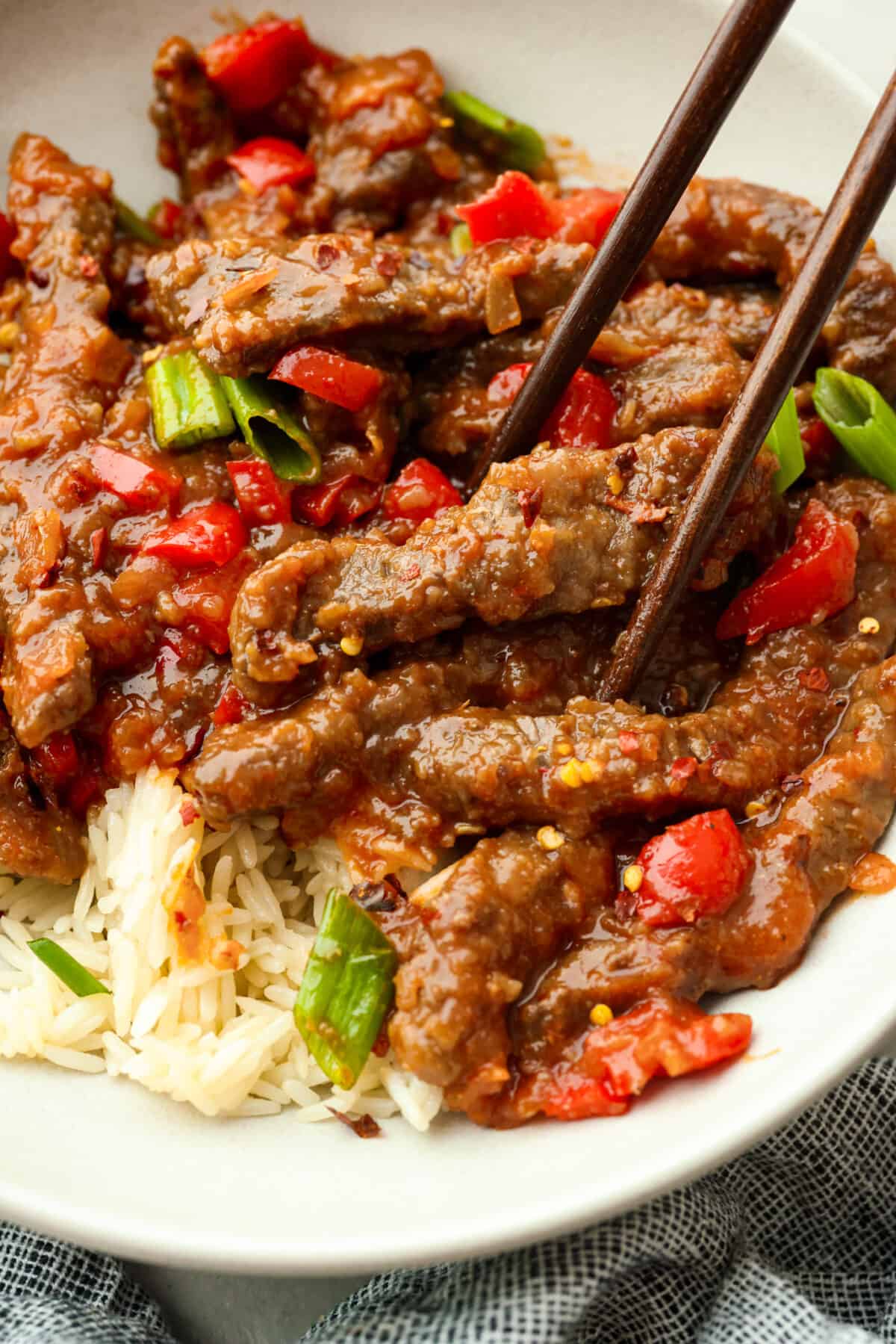 Crispy beef strips stir-fried with onion and red bell peppers then tossed in a sweet and tangy sauce. You're going to love this popular Panda Express copycat version of Beijing beef! Close view of chopsticks lifting up Beijing beef from a bowl.