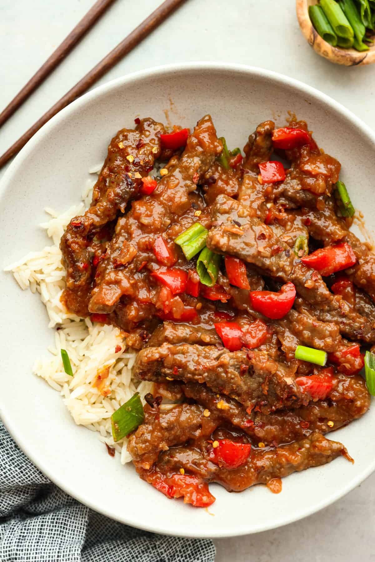 Crispy beef strips stir-fried with onion and red bell peppers then tossed in a sweet and tangy sauce. You're going to love this popular Panda Express copycat version of Beijing beef! Top view of Beijing beef in a white bowl over rice garnished with green onions.