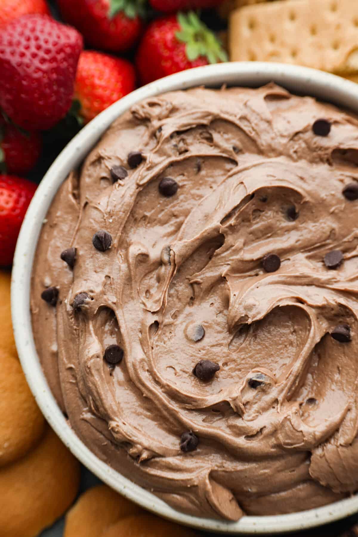 Brownie Batter Dip is an easy, delicious way to get all the brownie flavor without the baking! In this dessert dip recipe, brownie mix, cream cheese, vanilla and whipped topping get combined together for one of the most incredible treats. Serve with cookies, fruit and marshmallows! Closeup of chocolate dip filled with mini chocolate chips.