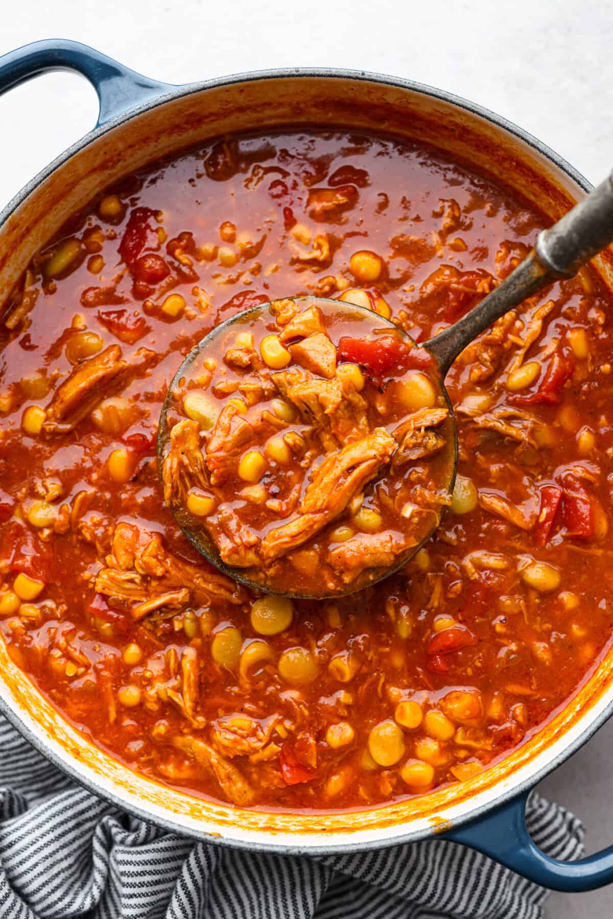 Brunswick stew has sizzling onions, garlic, BBQ sauce, and tender pulled pork all in one pot! Add a bit of cayenne for some zing and sweet corn and lima beans for texture. This combination of ingredients is so hearty and makes the best fall meal! Cooked Brunswick stew in a large pot, being scooped up with a ladle.