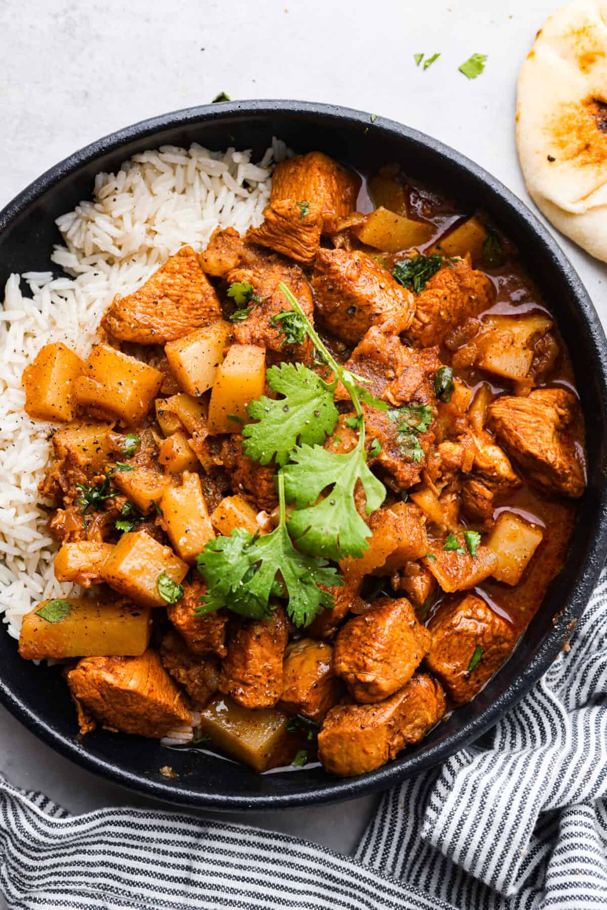 If youโve never had Chicken Vindaloo, youโre in for a treat! This classic Indian dish is made with chunks of marinated chicken and tender potatoes simmered in a tangy, flavorful, and perfectly spiced broth. Serve over fluffy white rice with Perfect Naan Bread for an irresistible, comforting meal! Instant Pot instructions included! A serving of chicken vindaloo and white rice in a black bowl.