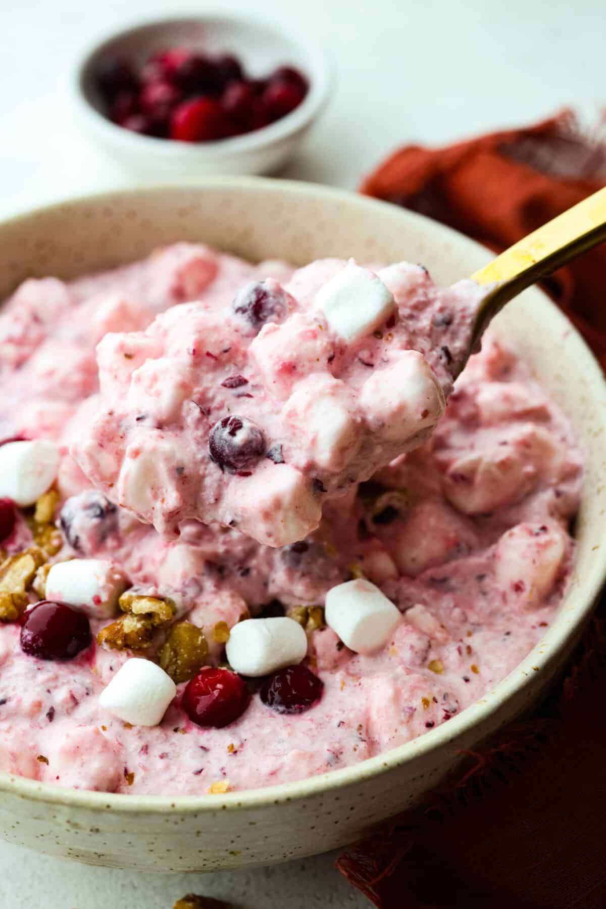 Cranberry Cheesecake Fluff is aย creamy and delicious fluff salad made with cranberries and walnuts. It is so easy to make and a MUST for the holidays! Mixing the topping and fluff together with a golden metal spoon.