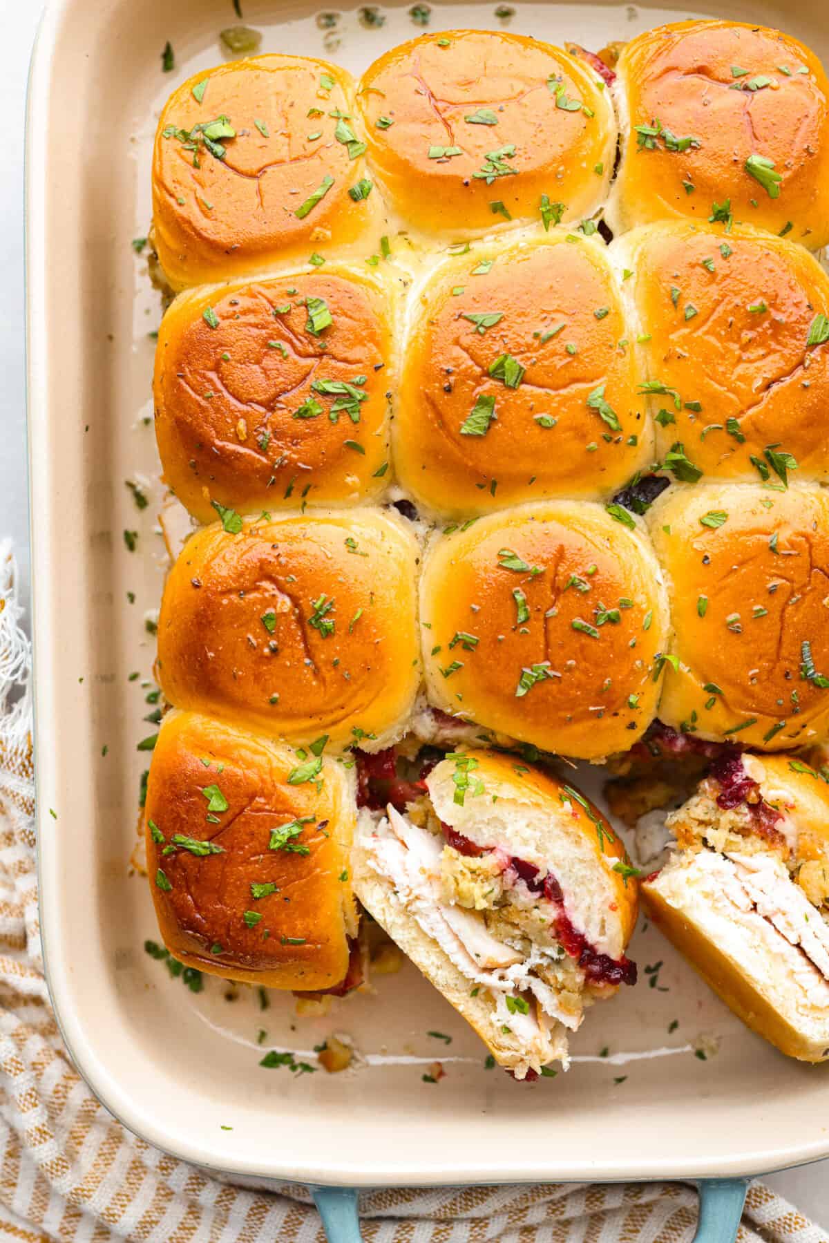 All the best things about Thanksgiving in slider form! These turkey cranberry sliders are warm and buttery, made with Hawaiian rolls packed full of turkey, stuffing, and cranberry sauce for the perfect balance of sweet and savory. A must-make with holiday leftovers! Top-down view of turkey cranberry sliders in a baking dish. Two are turned on their side so the filling can be seen.