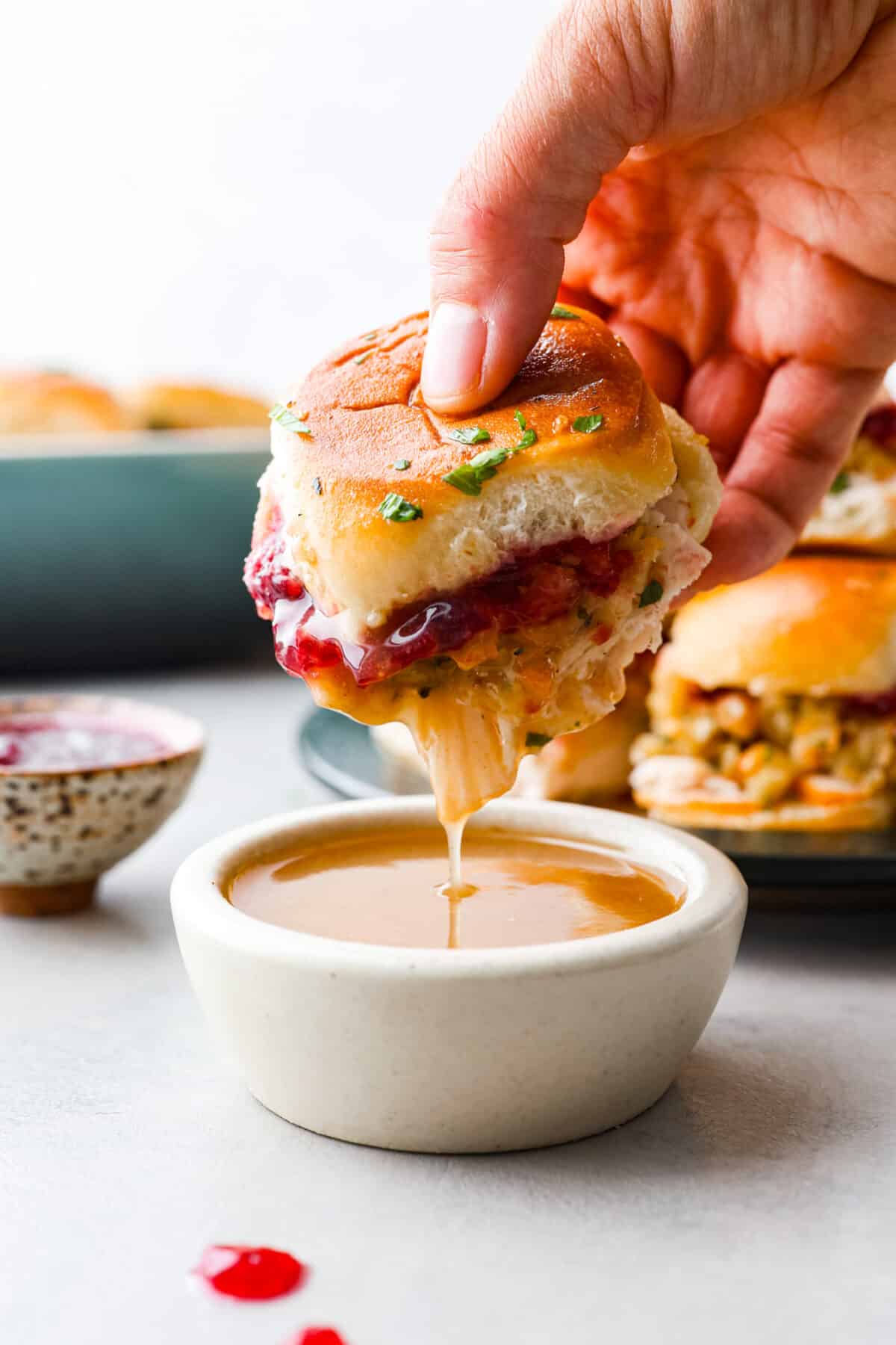 All the best things about Thanksgiving in slider form! These turkey cranberry sliders are warm and buttery, made with Hawaiian rolls packed full of turkey, stuffing, and cranberry sauce for the perfect balance of sweet and savory. A must-make with holiday leftovers! Dipping a slider into gravy.