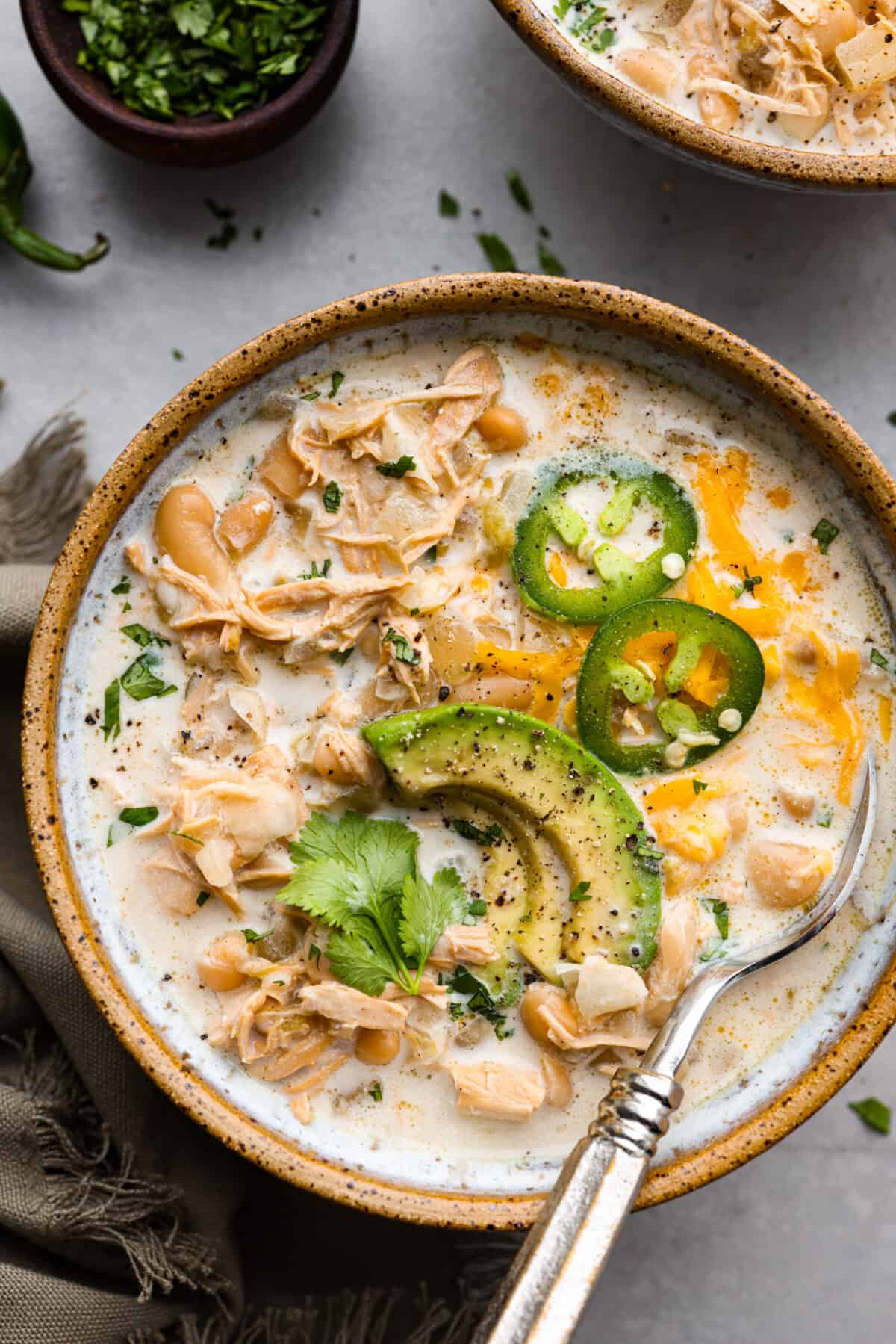 Crockpot White Chicken Chili combines chopped onions, garlic, spices, rotisserie chicken, green chiles, hearty beans, and chicken broth. The best part is the flavors meld in your slow cooker while it cooks all day. The top view of crockpot white chicken chili in a bowl.