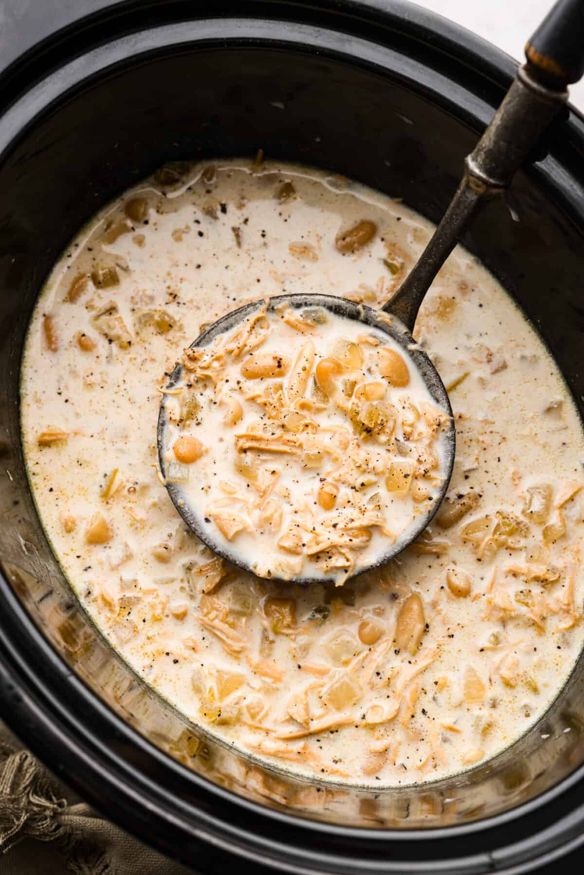 Crockpot White Chicken Chili combines chopped onions, garlic, spices, rotisserie chicken, green chiles, hearty beans, and chicken broth. The best part is the flavors meld in your slow cooker while it cooks all day. White chicken chili in a crockpot with a ladle.