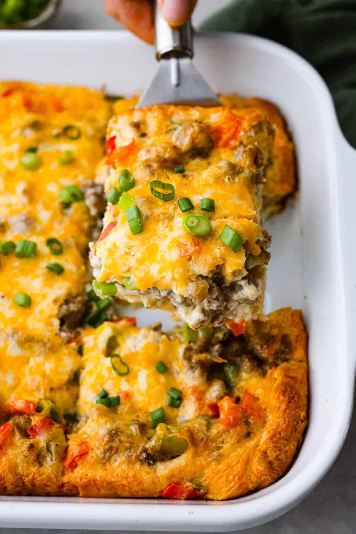 Meet crescent roll breakfast casserole: your new favorite way to use up that refrigerated crescent dough! Juicy pork sausage, eggs, chopped bell peppers, and shredded cheese get layered on top of that buttery, delicious crust. Easy to whip up in a snap, you're going to want to make it for breakfast all the time! Serving a piece of crescent roll breakfast casserole.