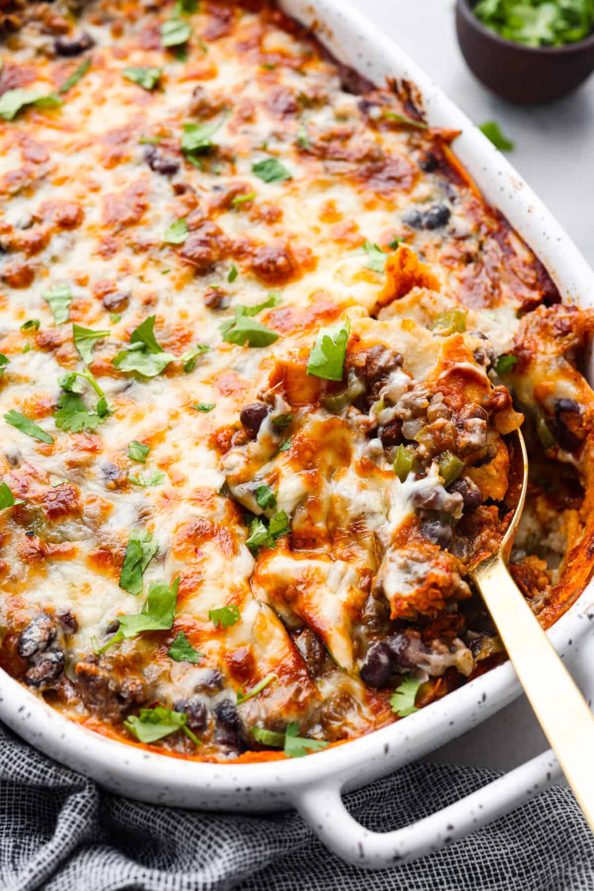 Enchilada Pie is layers of seasoned ground beef, veggies, beans, cheese, enchilada sauce, and corn tortillas; all baked together until perfectly cheesy and golden. This casserole recipe is an easy twist on enchiladas without the hassle of rolling! Hero image of enchilada casserole in a white baking dish.