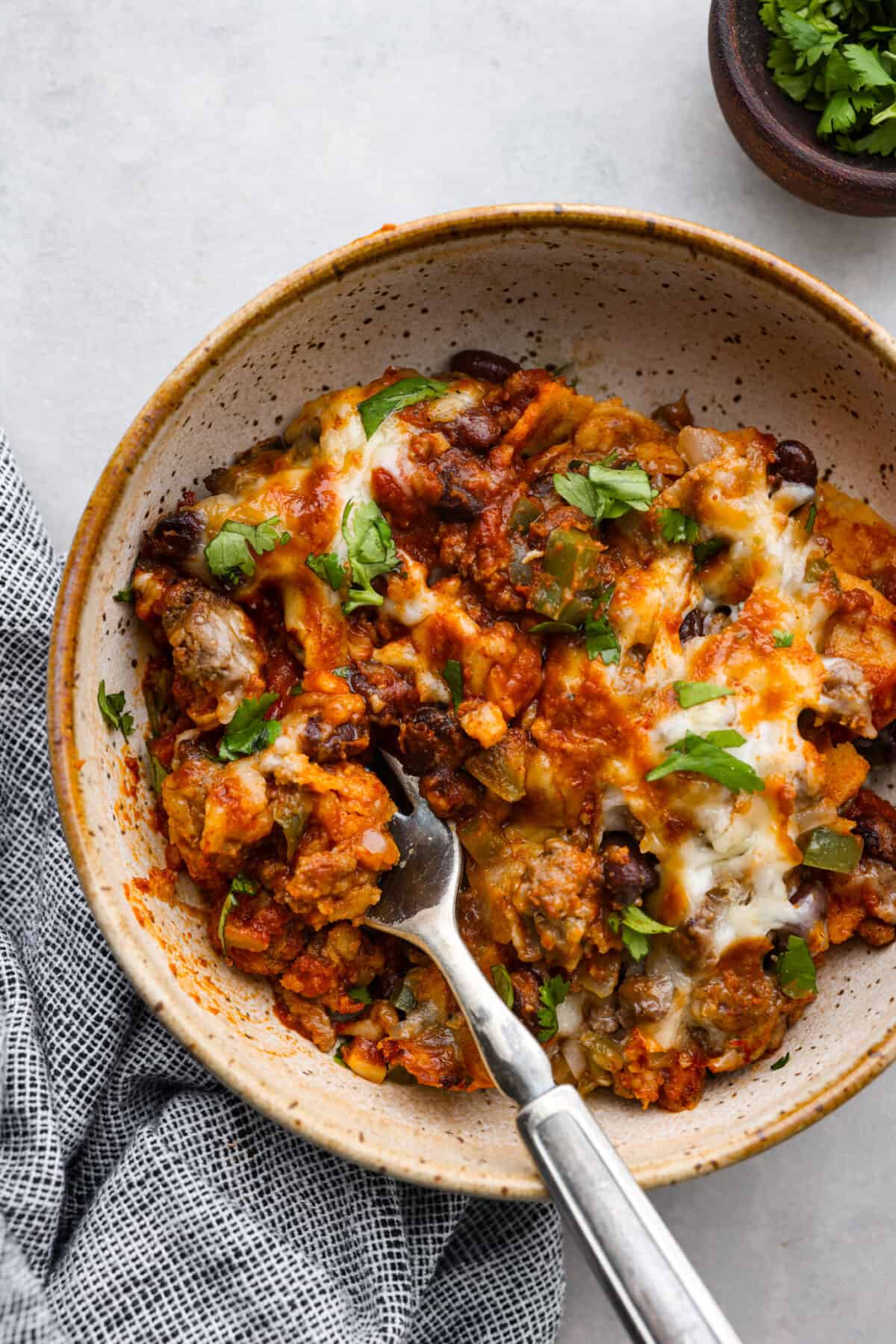 Enchilada Pie is layers of seasoned ground beef, veggies, beans, cheese, enchilada sauce, and corn tortillas; all baked together until perfectly cheesy and golden. This casserole recipe is an easy twist on enchiladas without the hassle of rolling! A serving of enchilada pie in a stoneware bowl.