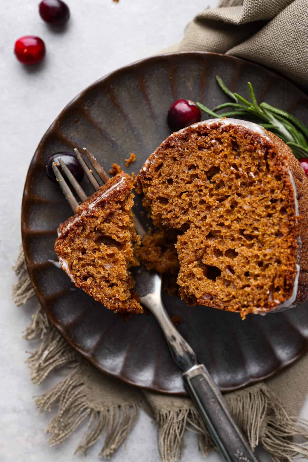 Festive Gingerbread Bundt Cake is moist, tender and the perfect dessert for the holidays. Topped with a flavorful brown butter maple glaze, youโll welcome a slice any time of day. Top-down view of a slice of gingerbread bundt cake on a black scalloped plate.