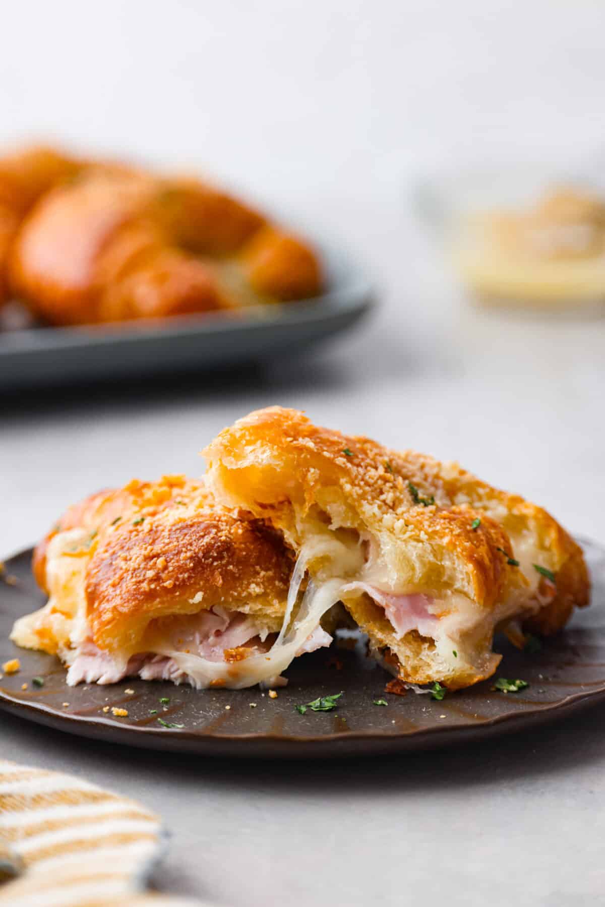 Get ready to devour the BEST ham and cheese croissant! Buttery warm croissants filled with a combination of melty cheeses and thinly sliced ham. These easy-to-make croissant sandwiches are perfect any time of day. Close view of a ham and cheese croissant cut in half on a brown plate.